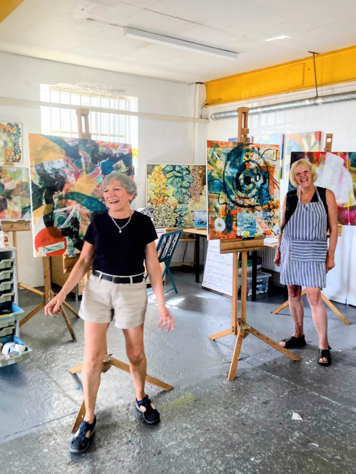 two women standing by their abstract paintings laughin and smiling