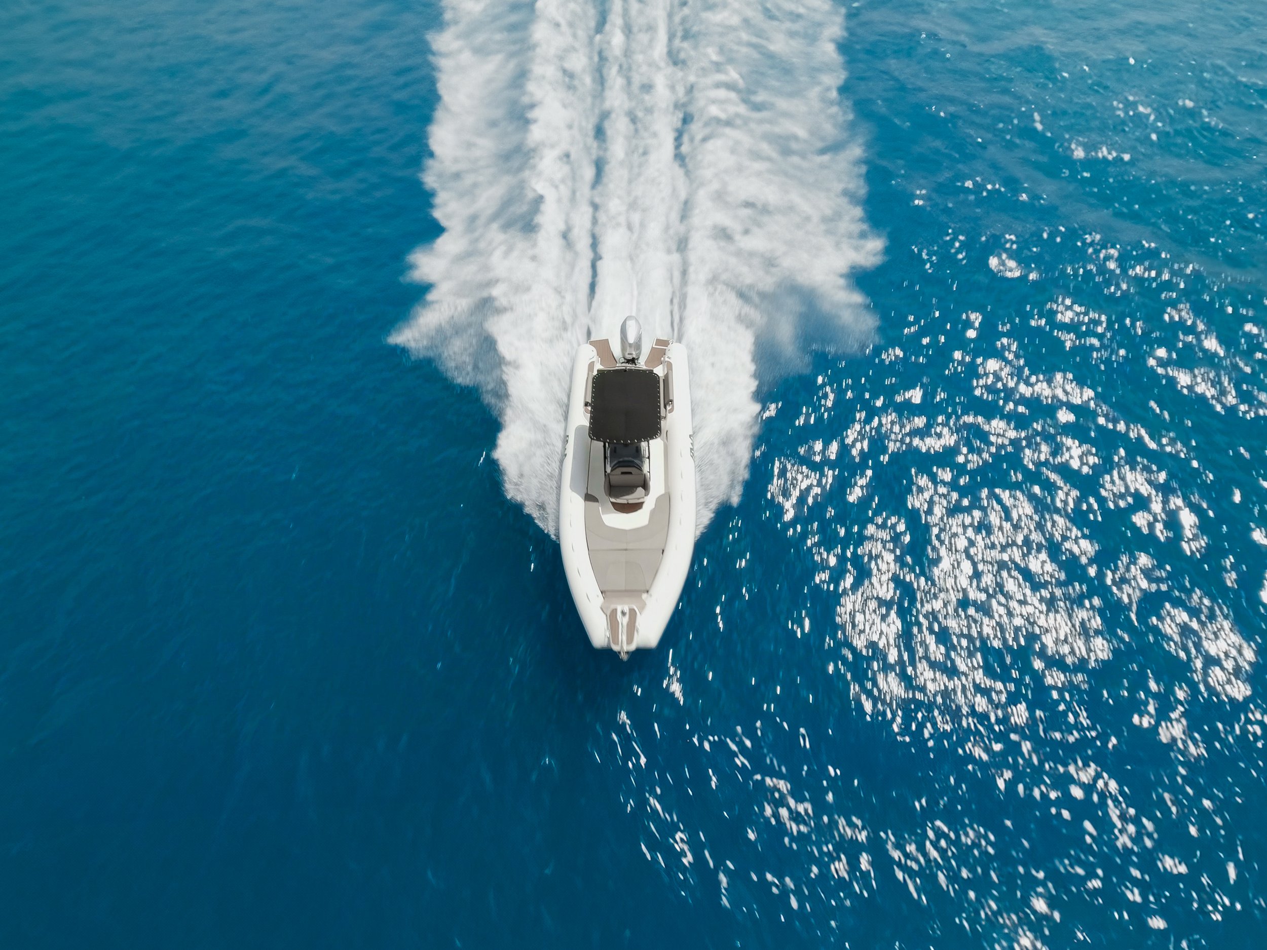 A white motorboat speeding through deep blue ocean water, creating a trail of foamy wake behind it.