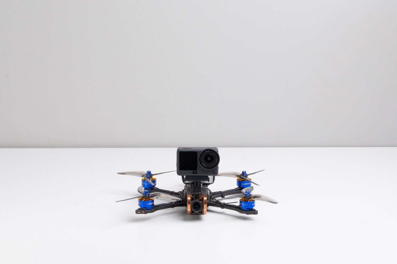 A racing drone with a mounted GoPro camera on top, placed on a white surface against a plain light gray background.