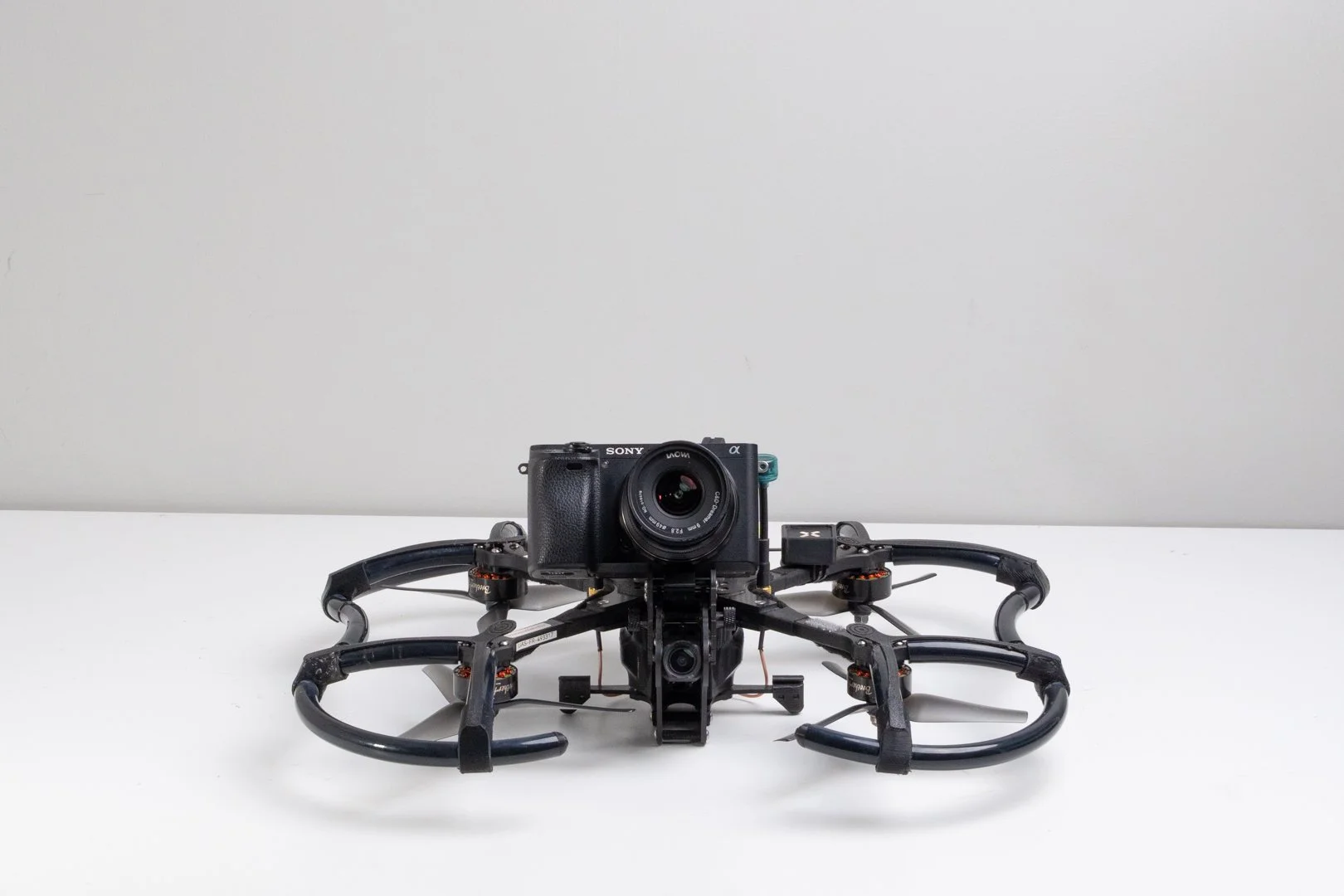 A drone with a mounted camera on a white surface against a gray wall.