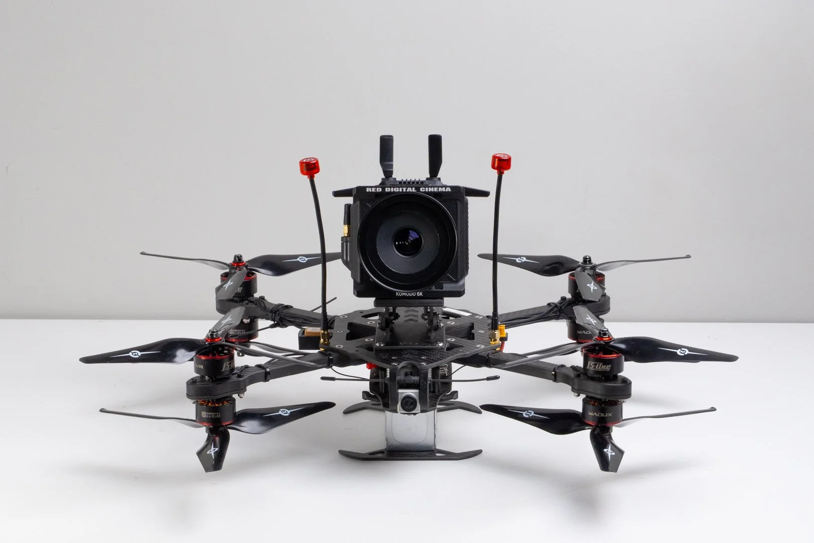 An FPV quadcopter drone with a professional camera mounted on top, placed on a white surface against a plain gray background. Heavy Lift Red Komodo Drone FPV