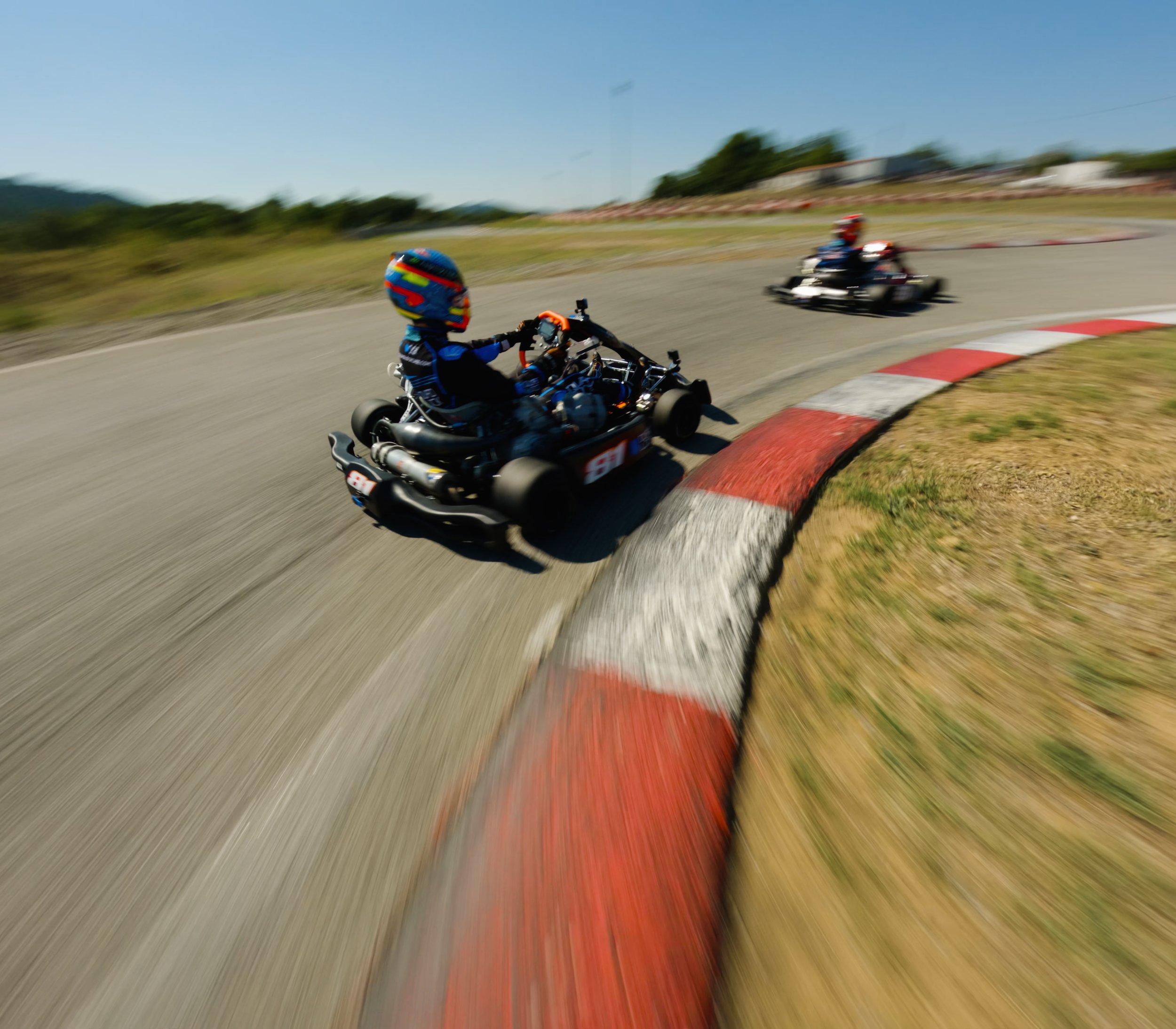 Two go-karts racing on a track, with the one in the foreground taking a turn, blurred background indicating speed.
