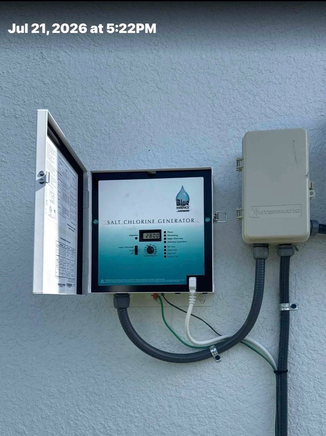 A salt chlorinator control box mounted on a textured white wall, displaying a digital reading of 2800. The control panel has labels indicating functions related to salt chlorination, with electrical conduits connected to it.