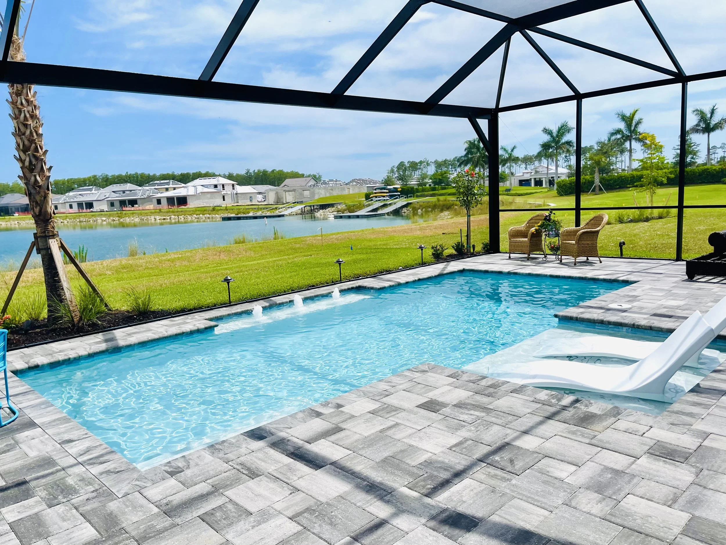 View from screened porch overlooking a swimming pool with a lake beyond, trees, and residential houses.