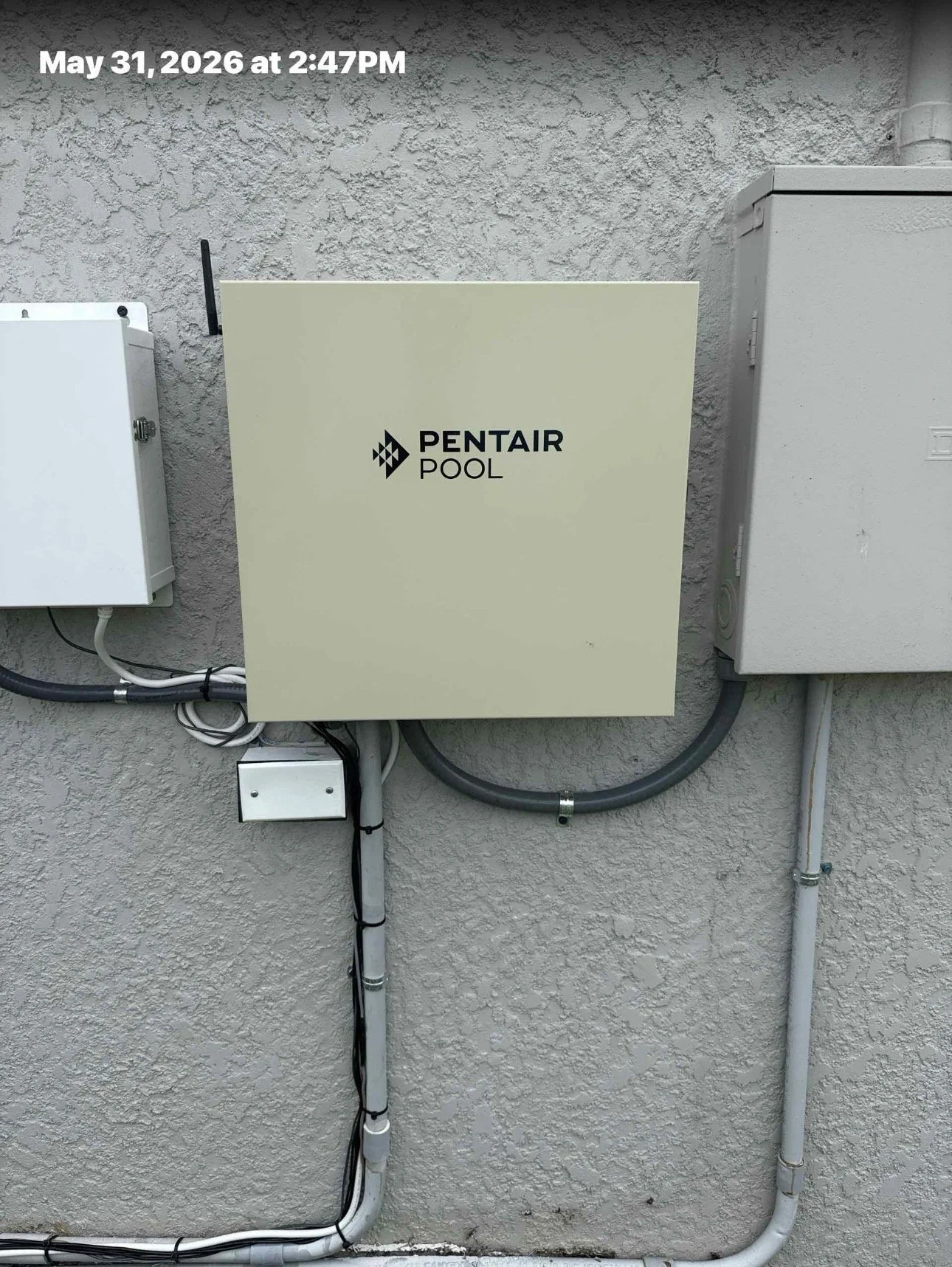 Electrical and plumbing utility boxes mounted on a stucco wall, with cables and pipes running vertically and horizontally.