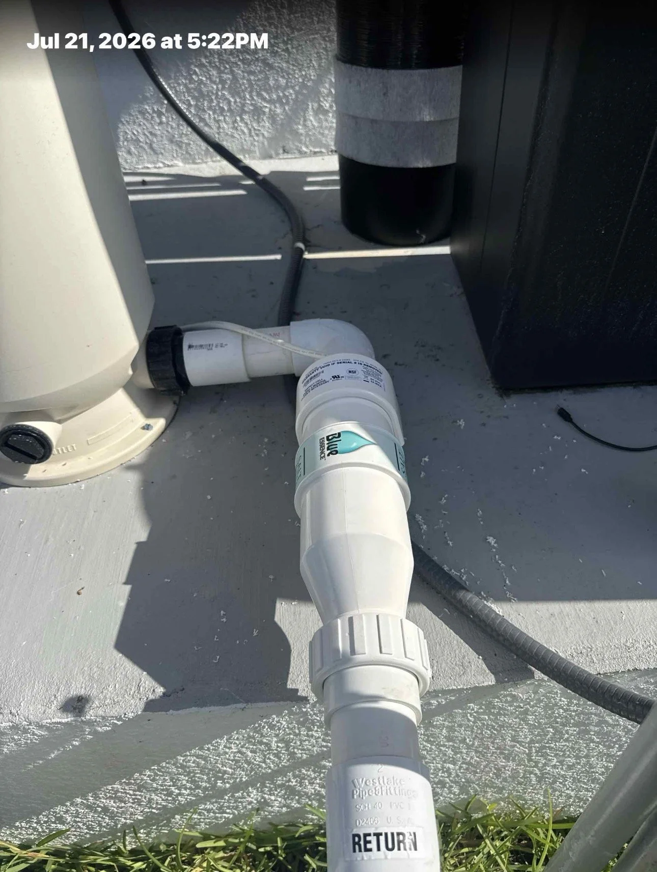 A white PVC pipe with a 'RETURN' label connected to a plumbing system on a building rooftop, with a black cylindrical object, a black cable, and a white textured wall in the background, and the date and time "Jul 21, 2026, 5:22 PM" at the top left.