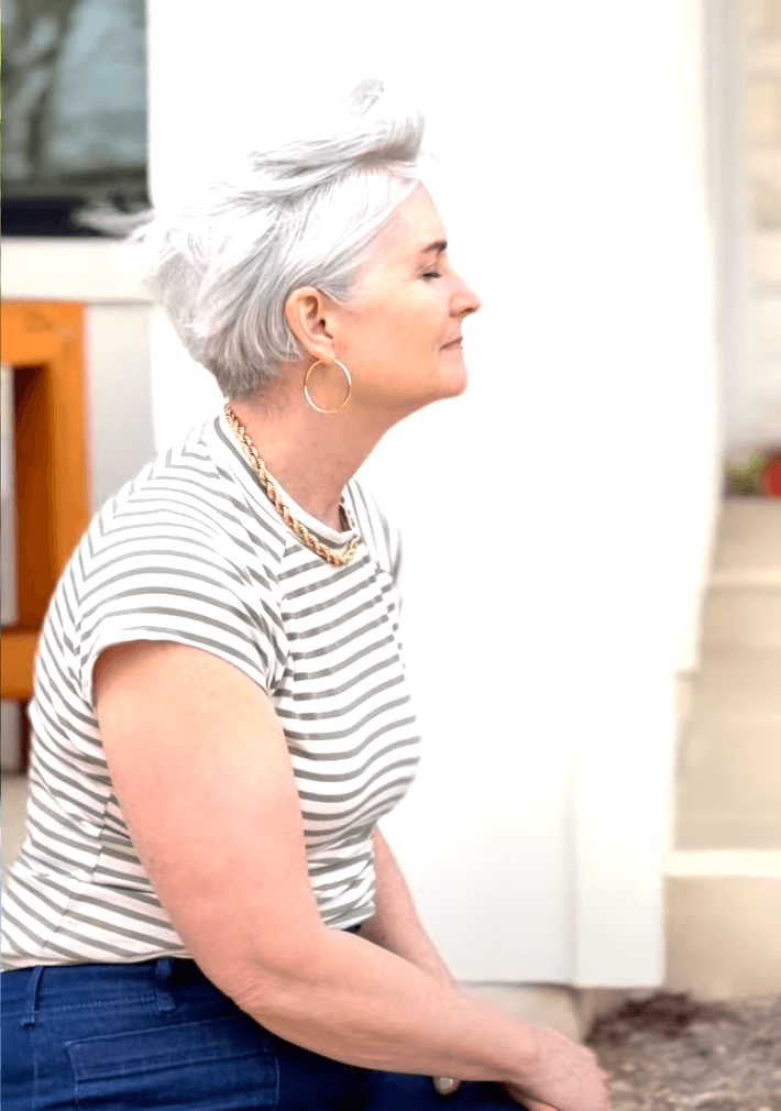 Christina sits, sideways, with her eyes slosed, wearing gold jewelry and a striped top