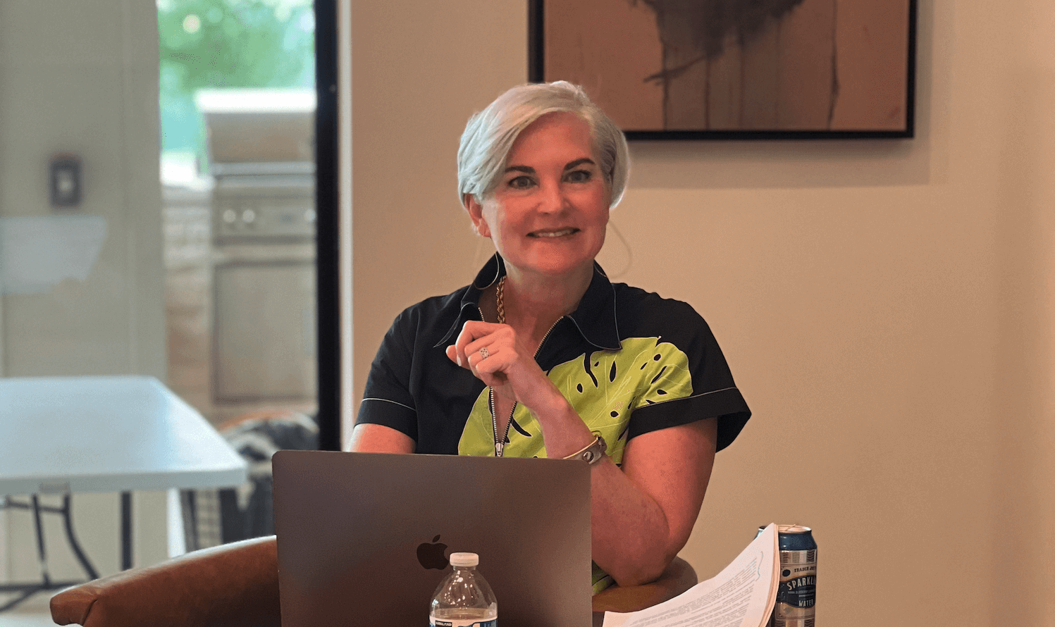 Christina sits in a leather chair, leading a consulting session, her laptop rests on her lap and her elbow is poised on the arm rest. She looks intently at someone asking a question.