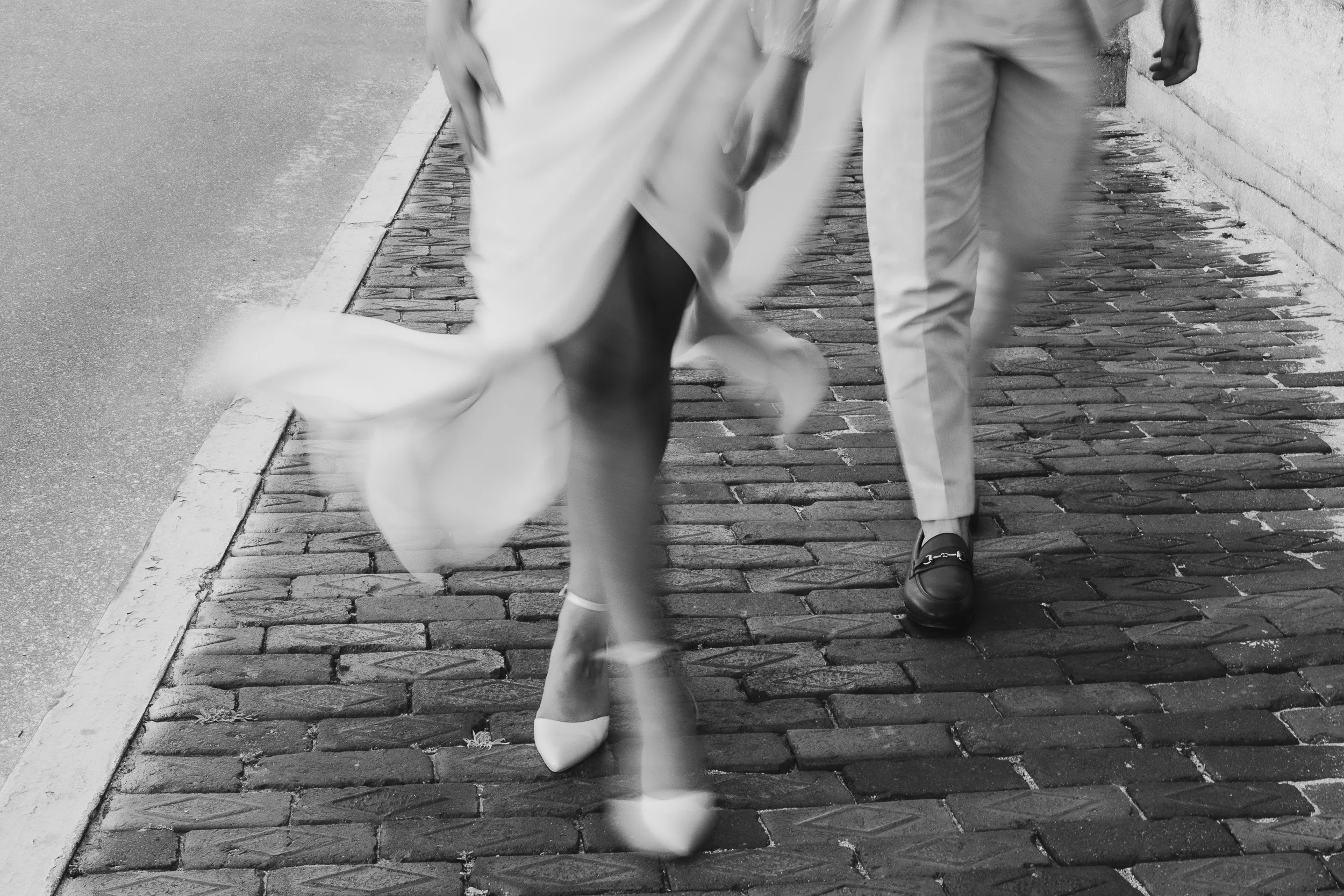 Close-up of a man walking on a brick sidewalk, wearing light-colored pants and black shoes, with a woman in motion ahead of him during elopement in Greenville SC