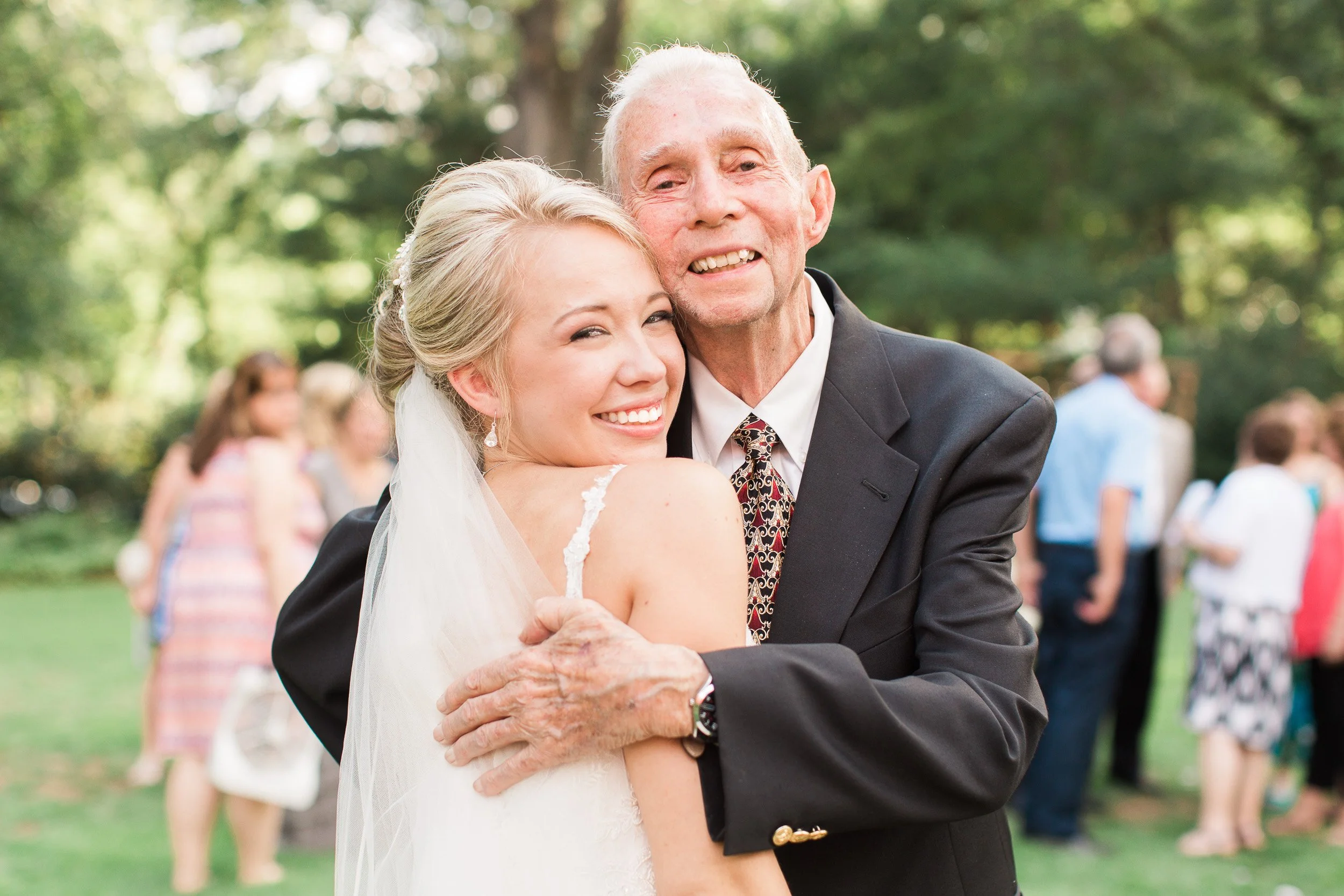 A bride and an elderly man, likely her grandfather, sharing a hug at an outdoor wedding. The bride is smiling with her eyes closed, and the man is smiling broadly during intimate wedding at Lake Keowee in South Carolina