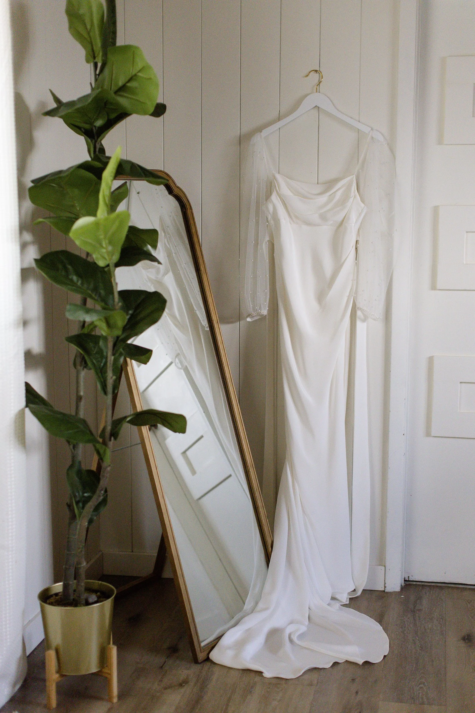 A wedding dress hanging on a white wall with a full-length mirror during small wedding in downtown Greenville, SC