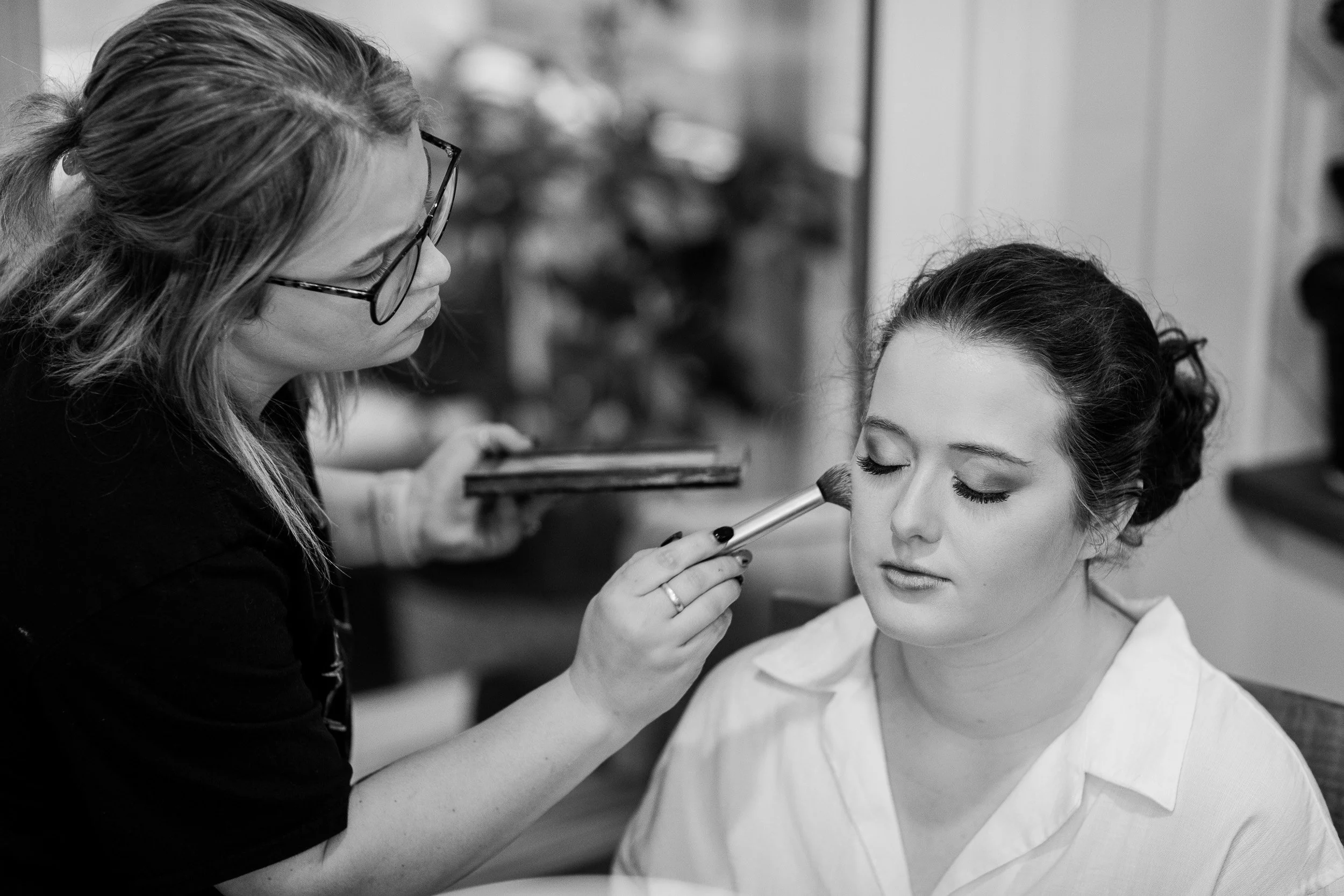 A makeup artist applying makeup on a woman's face in a salon setting for intimate wedding in Clemson, SC