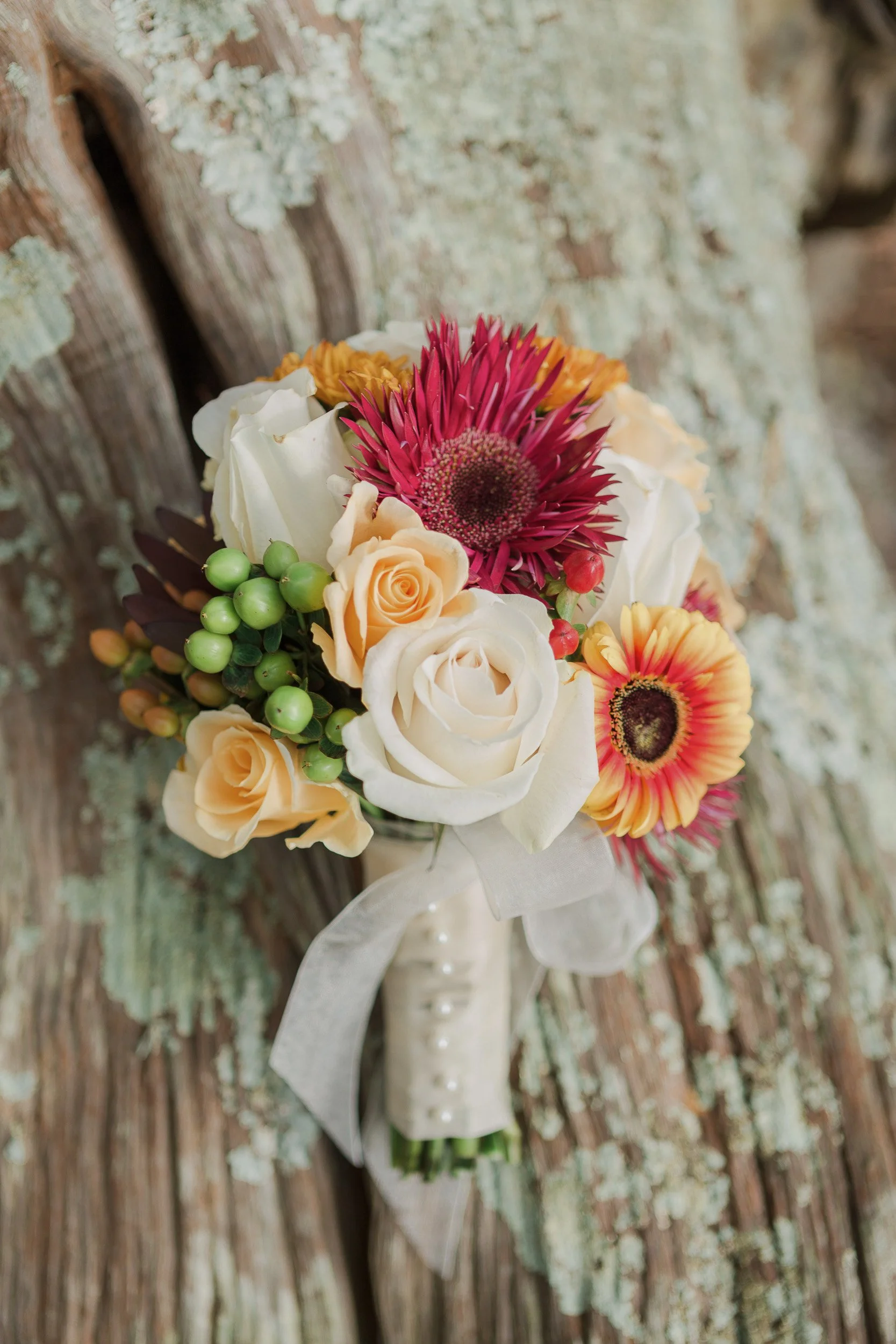 Close-up of a bouquet of flowers resting on a rocky surface with green moss and lichen outdoors during elopement in Greenville, SC