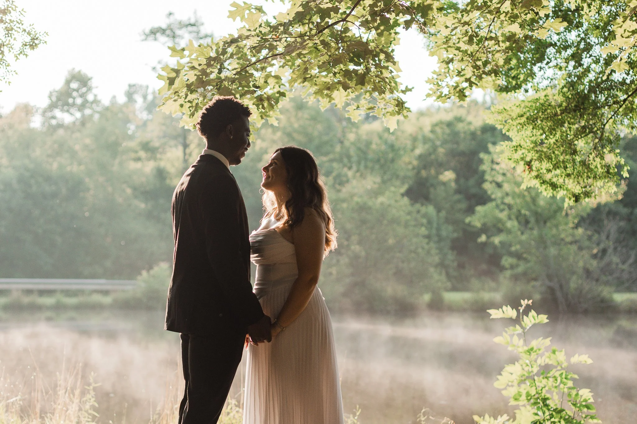 A couple sharing an intimate moment outdoors under a tree, facing each other and holding hands, with sunlight filtering through the foliage or intimate wedding in Clemson SC