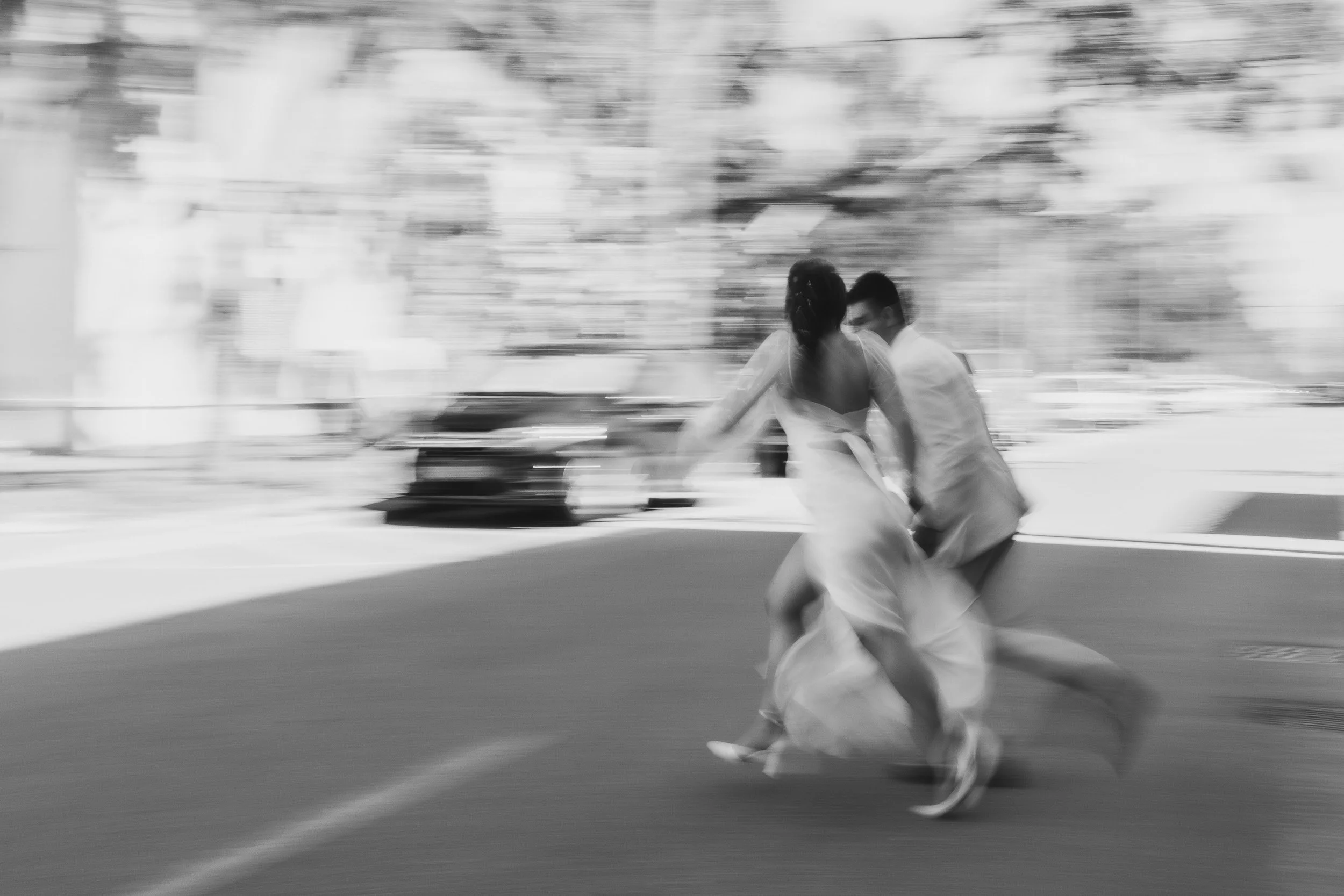 A black and white photograph of a couple in wedding attire walking outside on a city street, with motion blur in the background during elopement in Greenville, SC