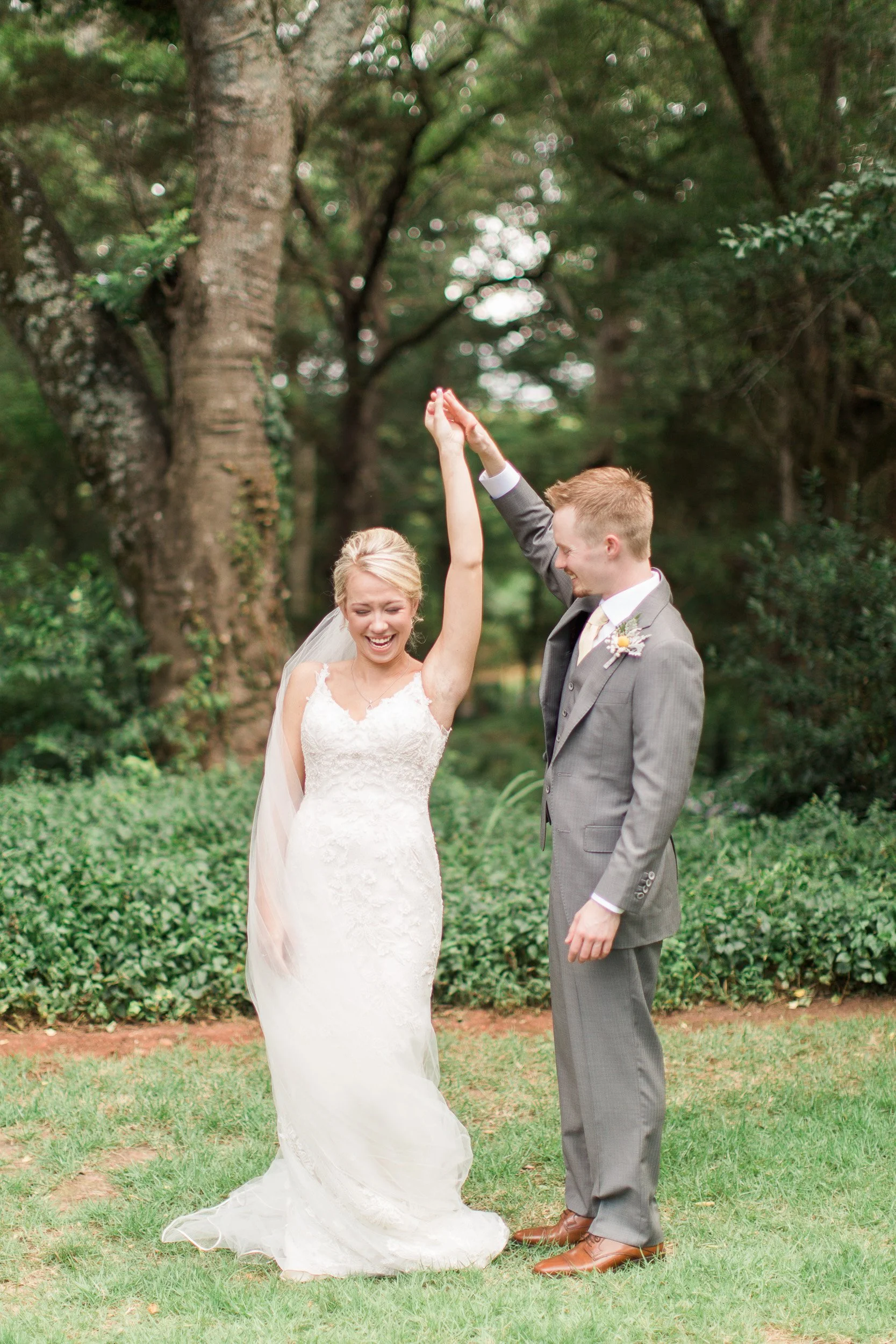 Bride and groom celebrating outdoors, with the bride raising her hand and the groom smiling, surrounded by trees and greenery at Sleepy Hollow Barn in Pendleton SC