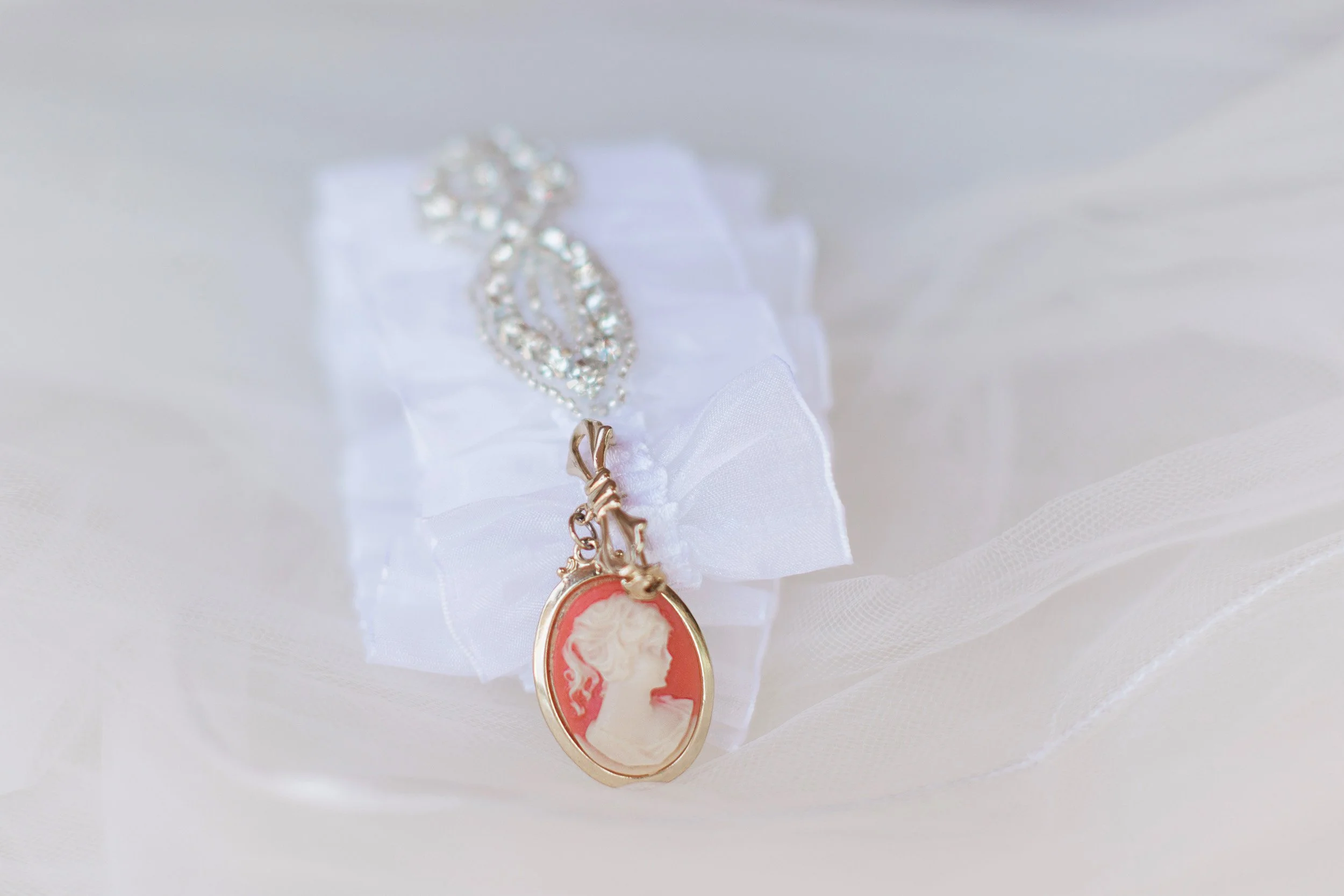 Close-up of a vintage cameo pendant with a profile of a woman's face, hanging on a chain, displayed on white fabric  before intimate wedding at Lake Keowee in South Carolina