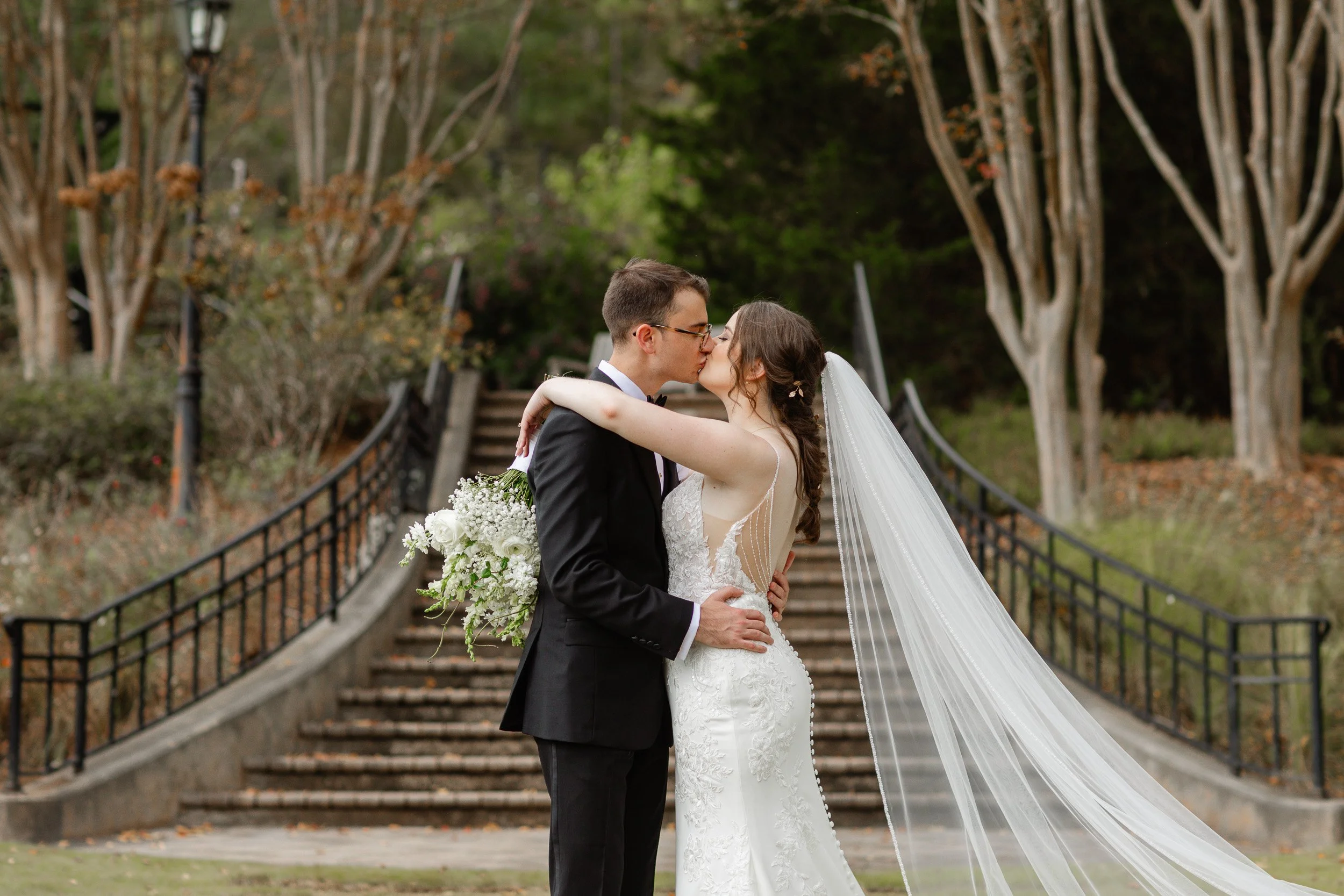A bride and groom kiss outdoors on stairs in a garden during intimate garden wedding in Greenville SC.
