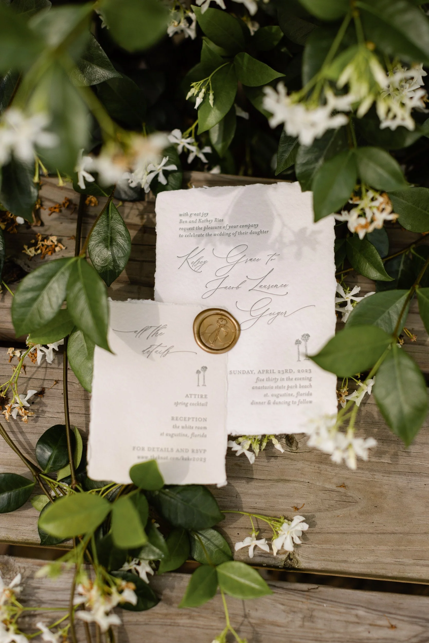 A wedding invitation card placed among green leaves and white flowers on a wooden surface in Greenville, SC