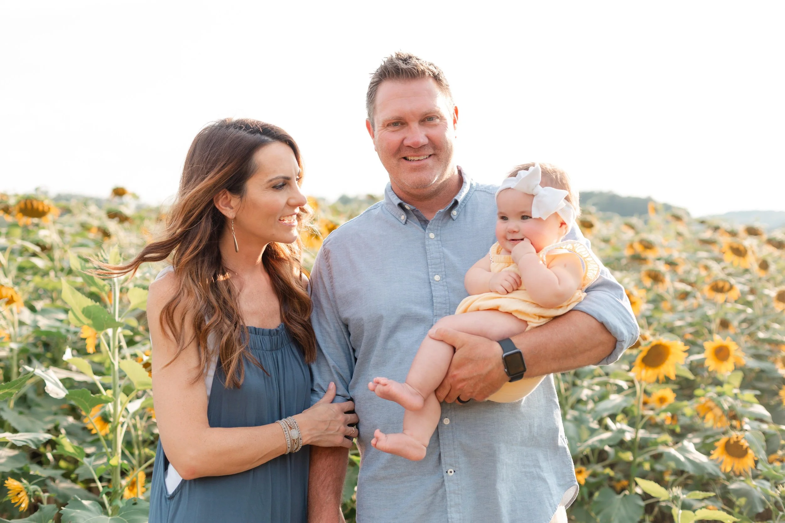 Family of three in sunflower field holding baby girl smiling at each other in Clemson SC