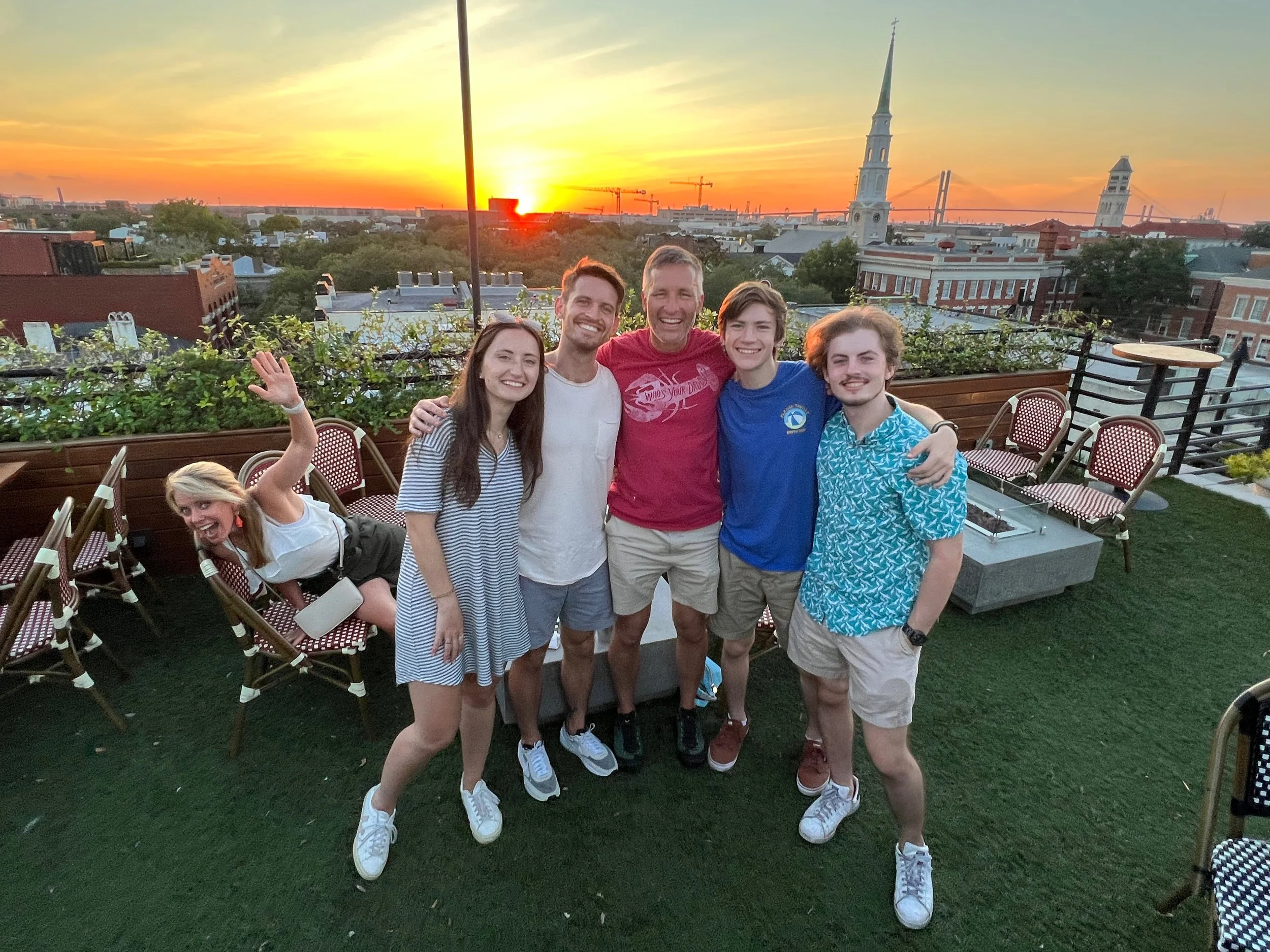 Kelly McAtee (far left) with family on a Savannah rooftop at sunset, with the Cathedral of St. John the Baptist in the background.