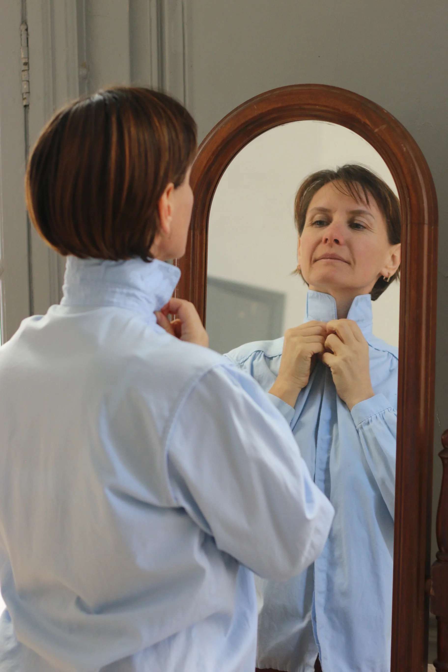 Femme se regardant dans un miroir en train de boutonner sa chemise