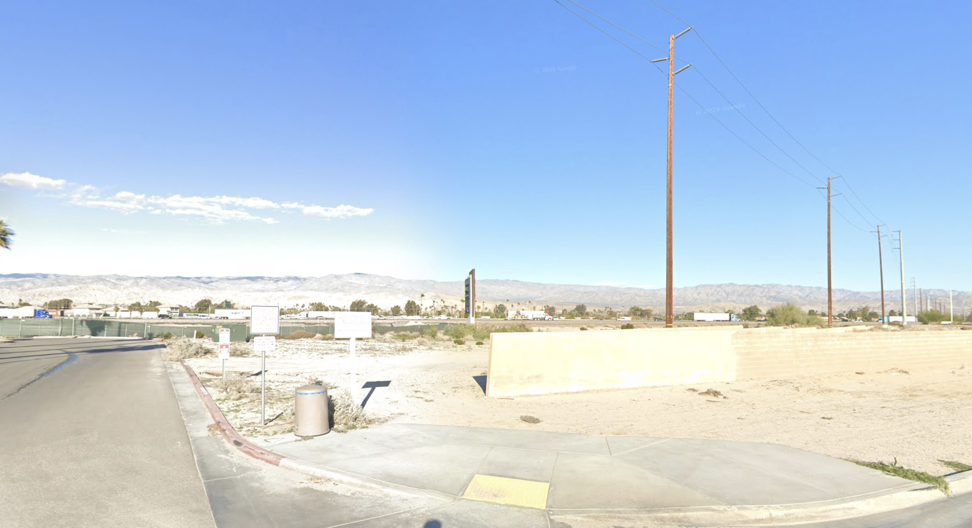 A desert road with utility poles and distant mountains under a clear blue sky.