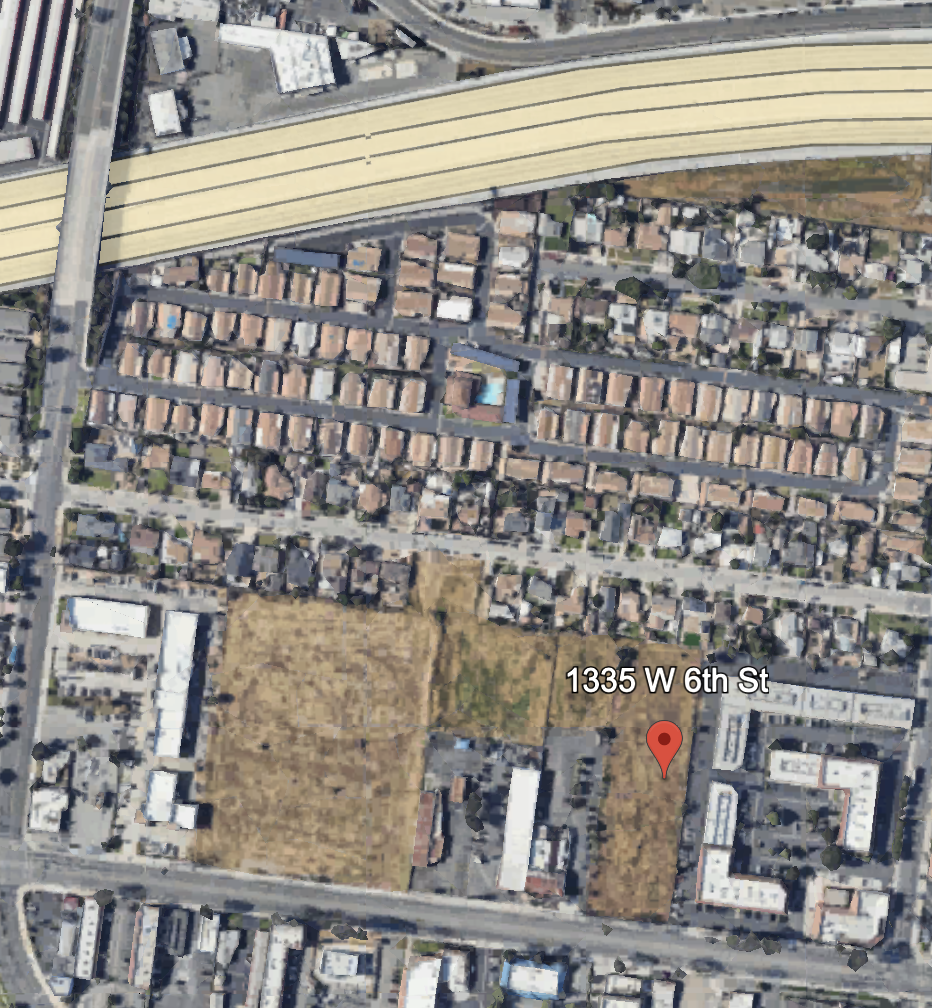 An aerial view of a residential neighborhood with a large highway or overpass at the top and a mix of houses and open lots below, including one property marked at 1355 W 6th St.