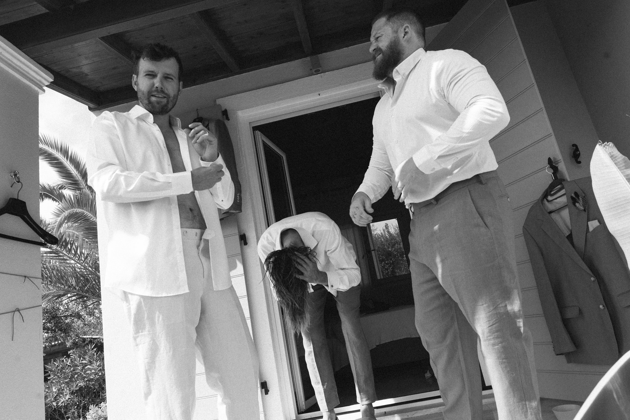 Three men and one woman inside a house, with some men adjusting their shirts and the woman covering her face, in a black-and-white photograph.