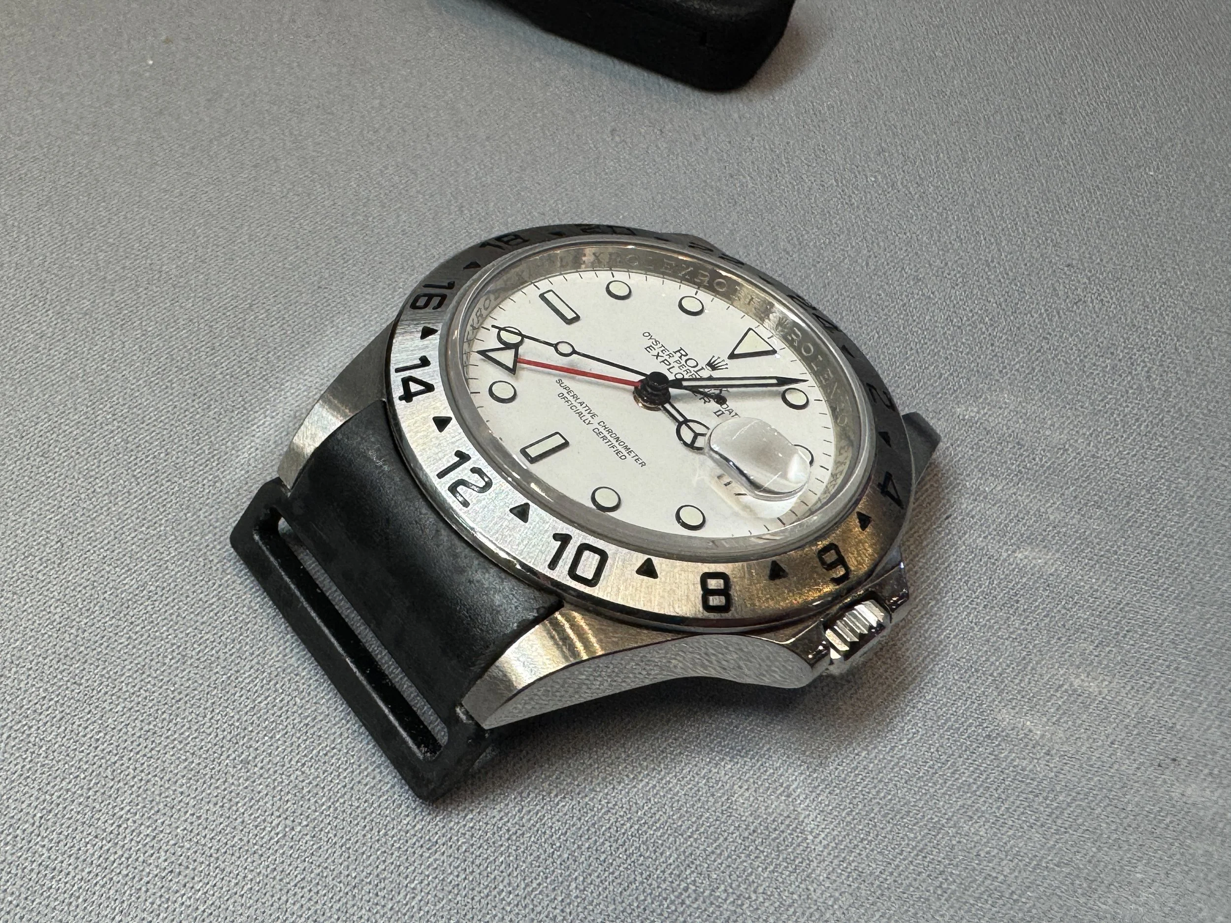 A wristwatch with a white dial, black hour markers, and a black strap on a gray textured surface.