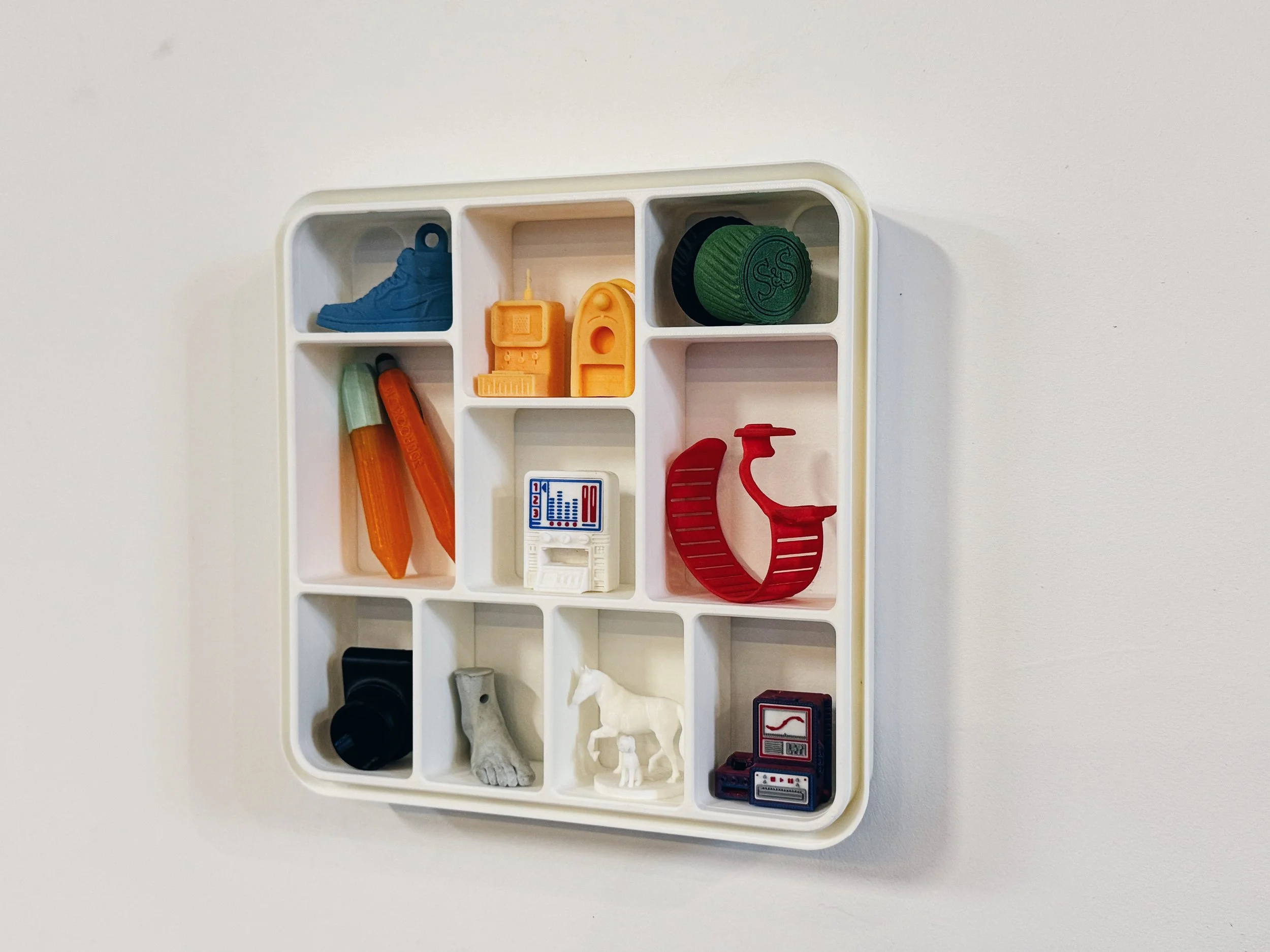 Plastic compartmentalized tray with miniature toy items including a blue sneaker, a yellow TV, green and black containers, an orange item, a red comb, a white horse, and miniature electronic devices.