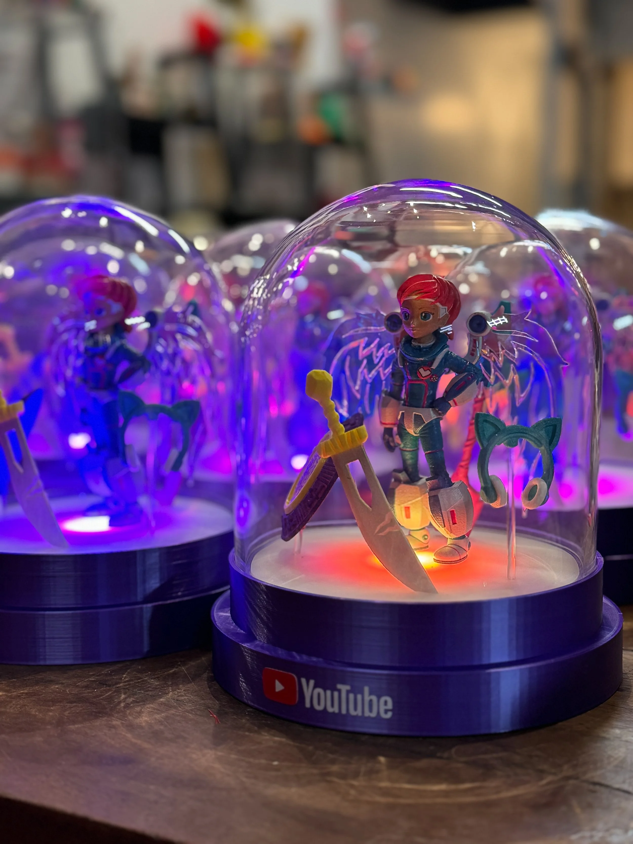A display of YouTube-themed snowglobes with character figurines illuminated with colorful lights.