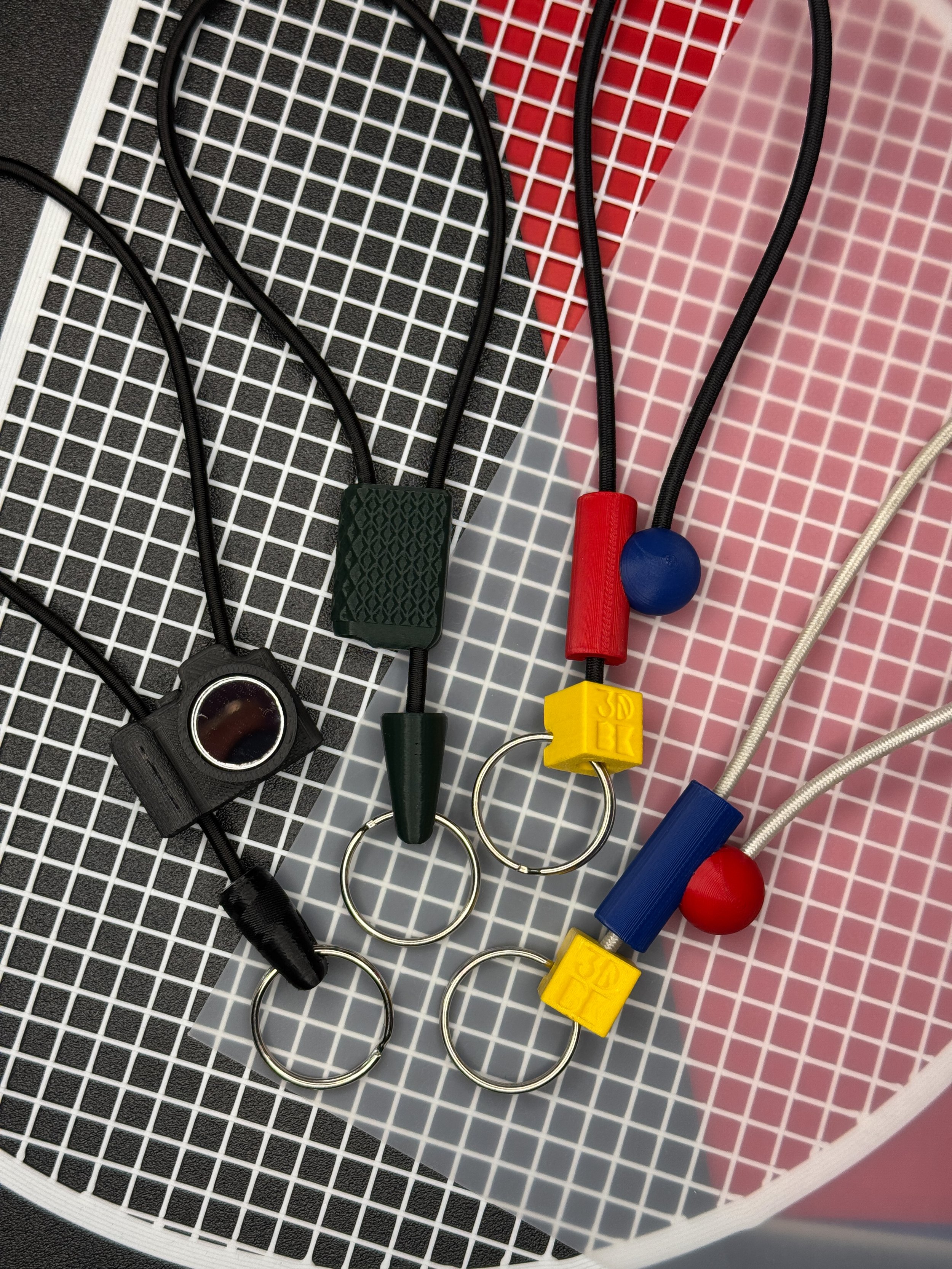 Various colored valve handles and keychains with black cords on a white and red grid-like surface.