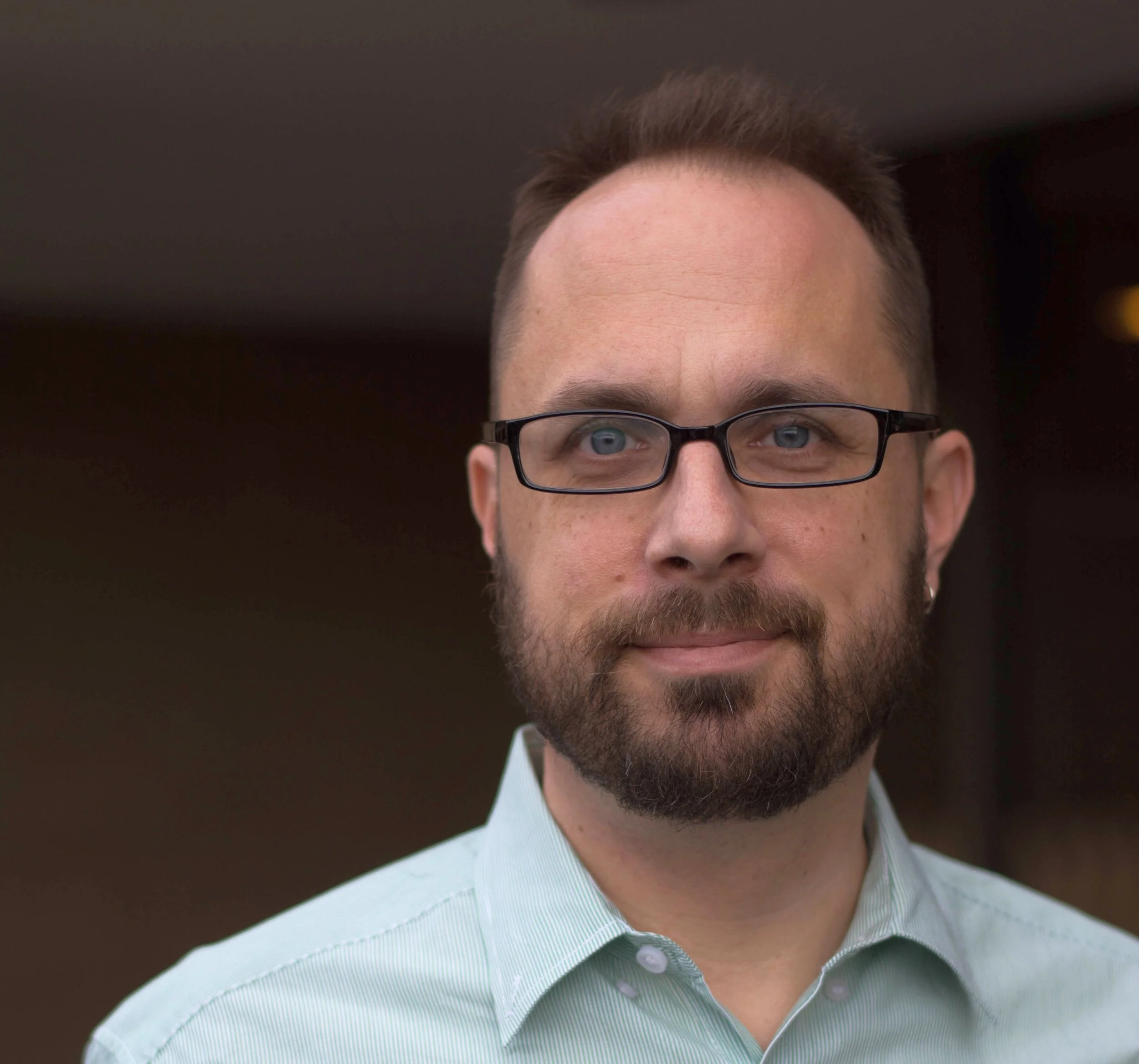 Ross White wearing glasses and a blue button up collared shirt.
