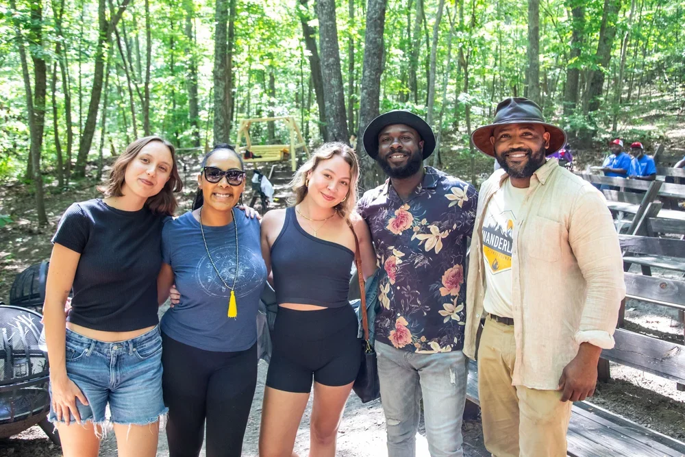 Group of five diverse friends standing together in a wooded park, smiling and posing for the camera.