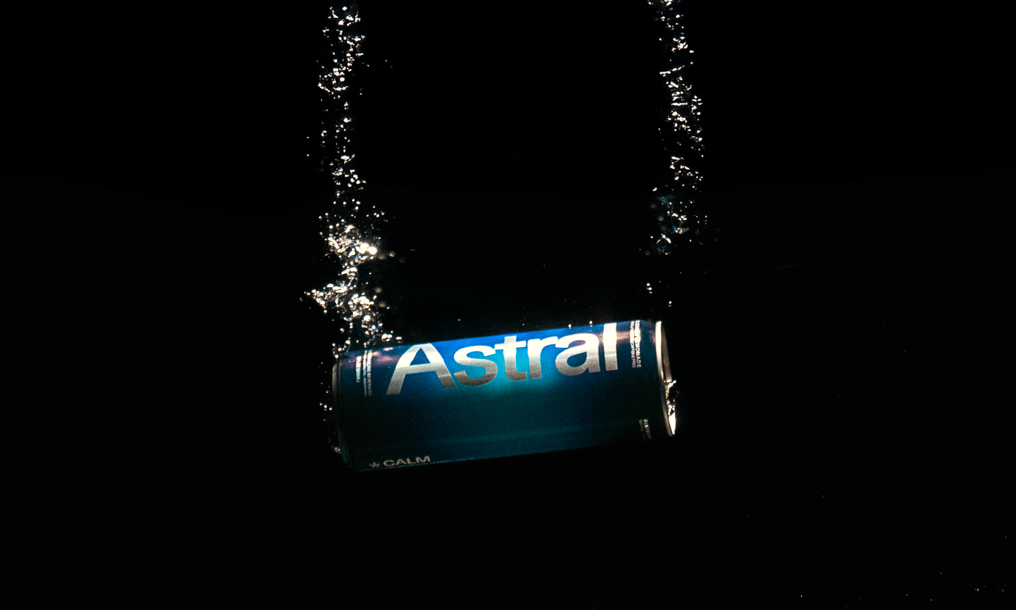 A blue can labeled 'Astral' floating on dark water with bubbles around it.