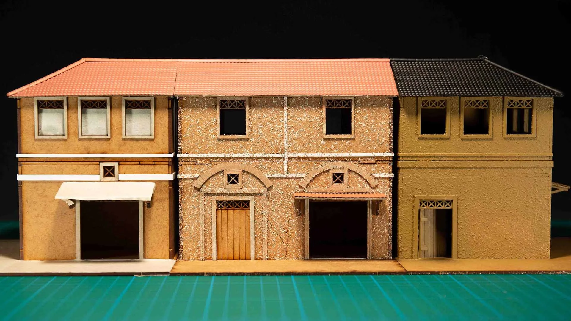 Three assembled MDF model buildings for miniature wargaming, showing applied wall textures and raw wood details before painting.