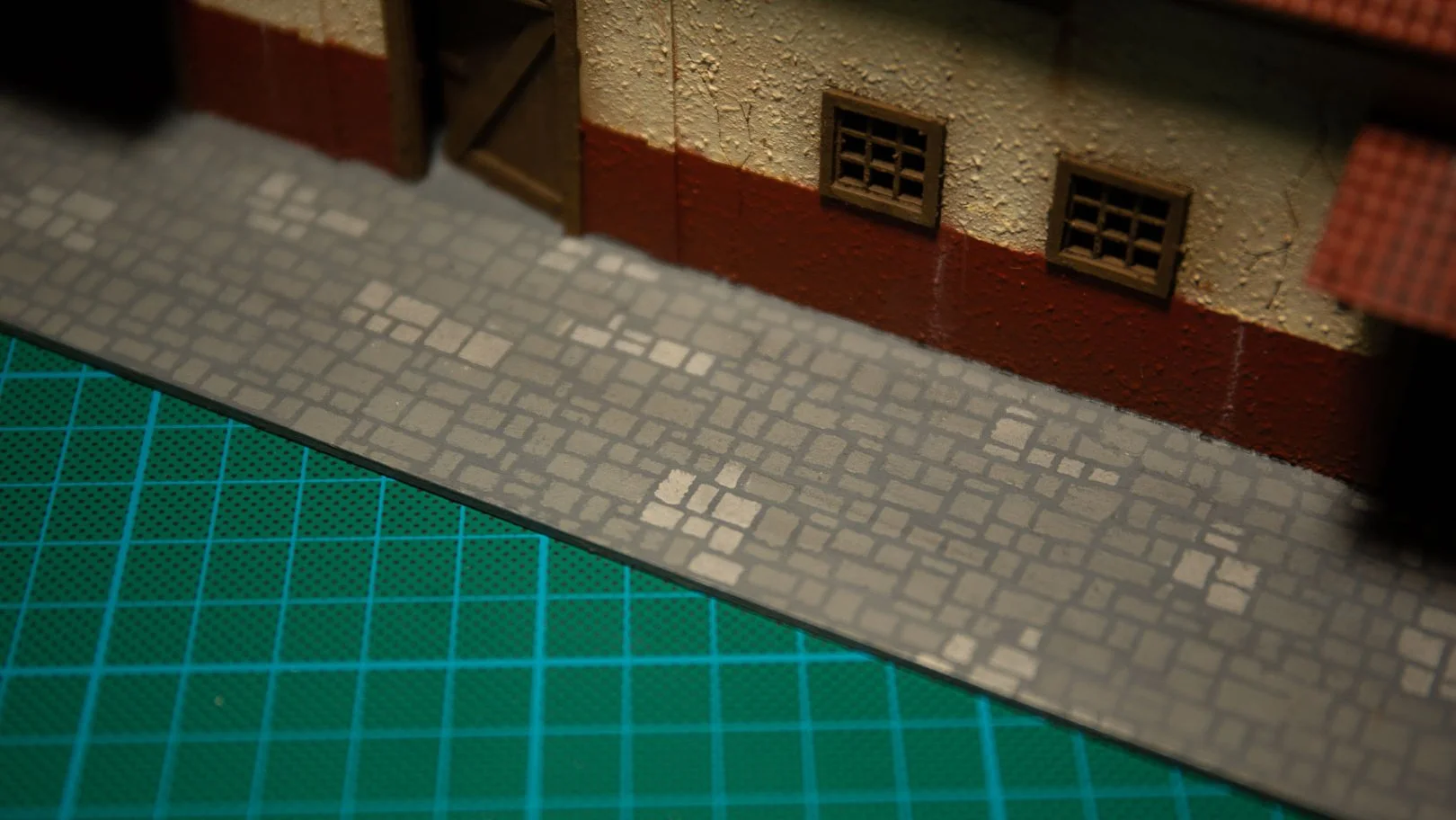 Close-up view of a painted cobblestone street texture applied to the base of an MDF miniature model building.