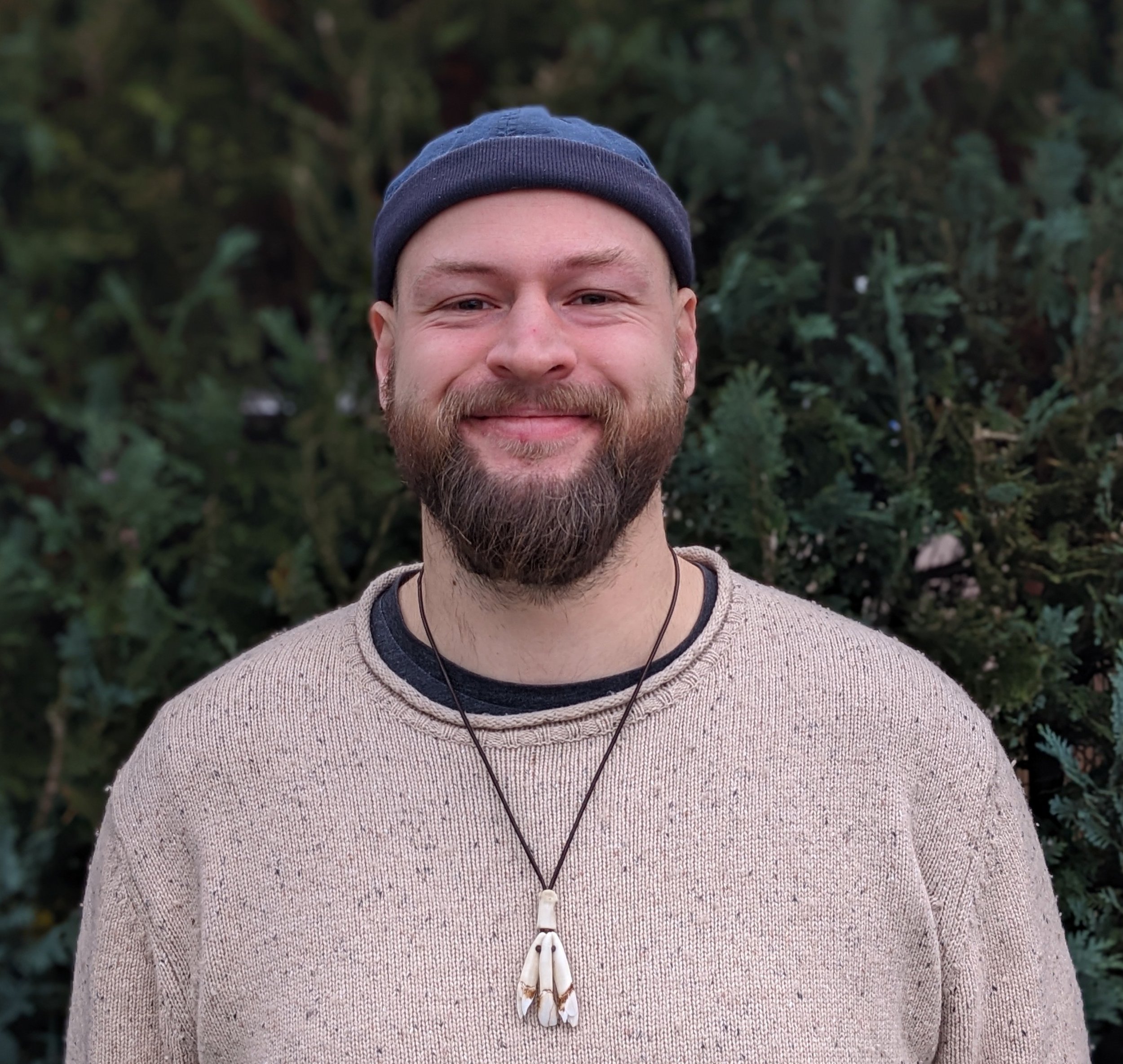 Ein Mann mit Helm und Kletterausrüstung sitzt in einem Baum in einem Wald, umgeben von grünen Blättern.