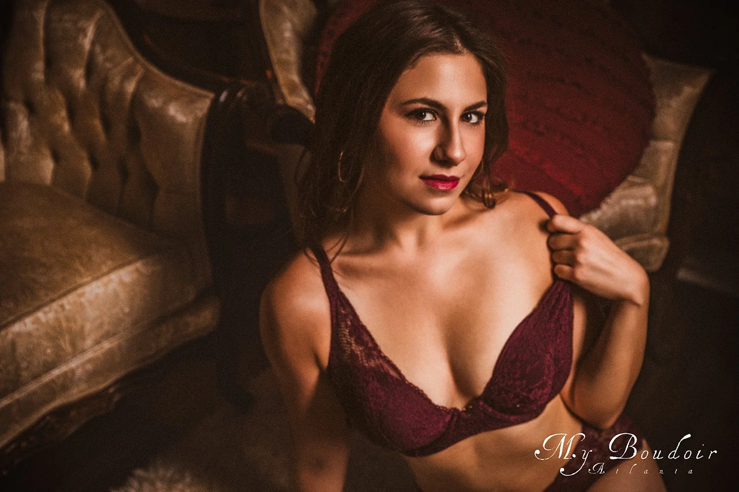 Woman wearing burgundy lingerie sitting on a vintage chair in a boudoir setting.