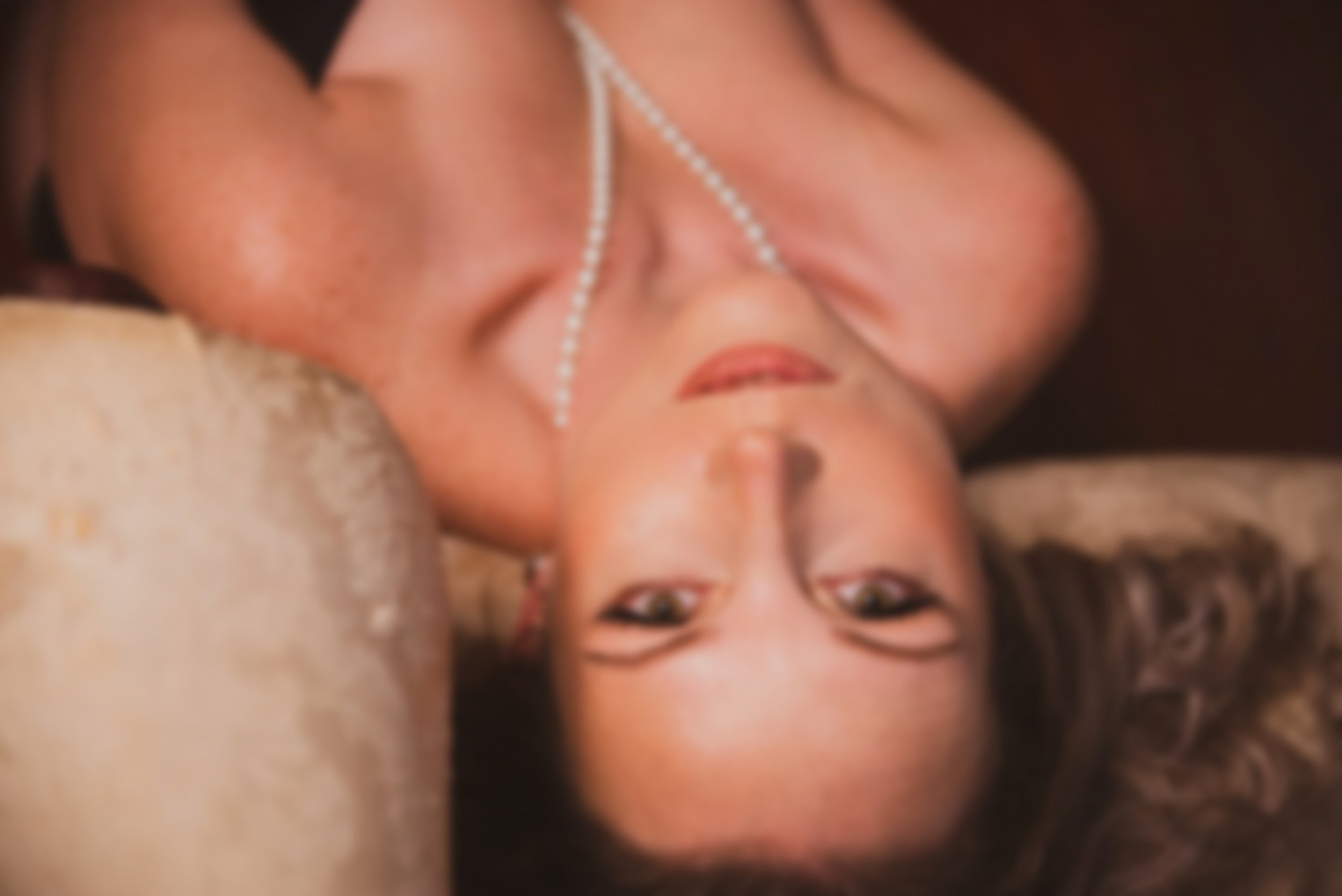 Woman with pearls looks directly into the camera for boudoir photoshoot.