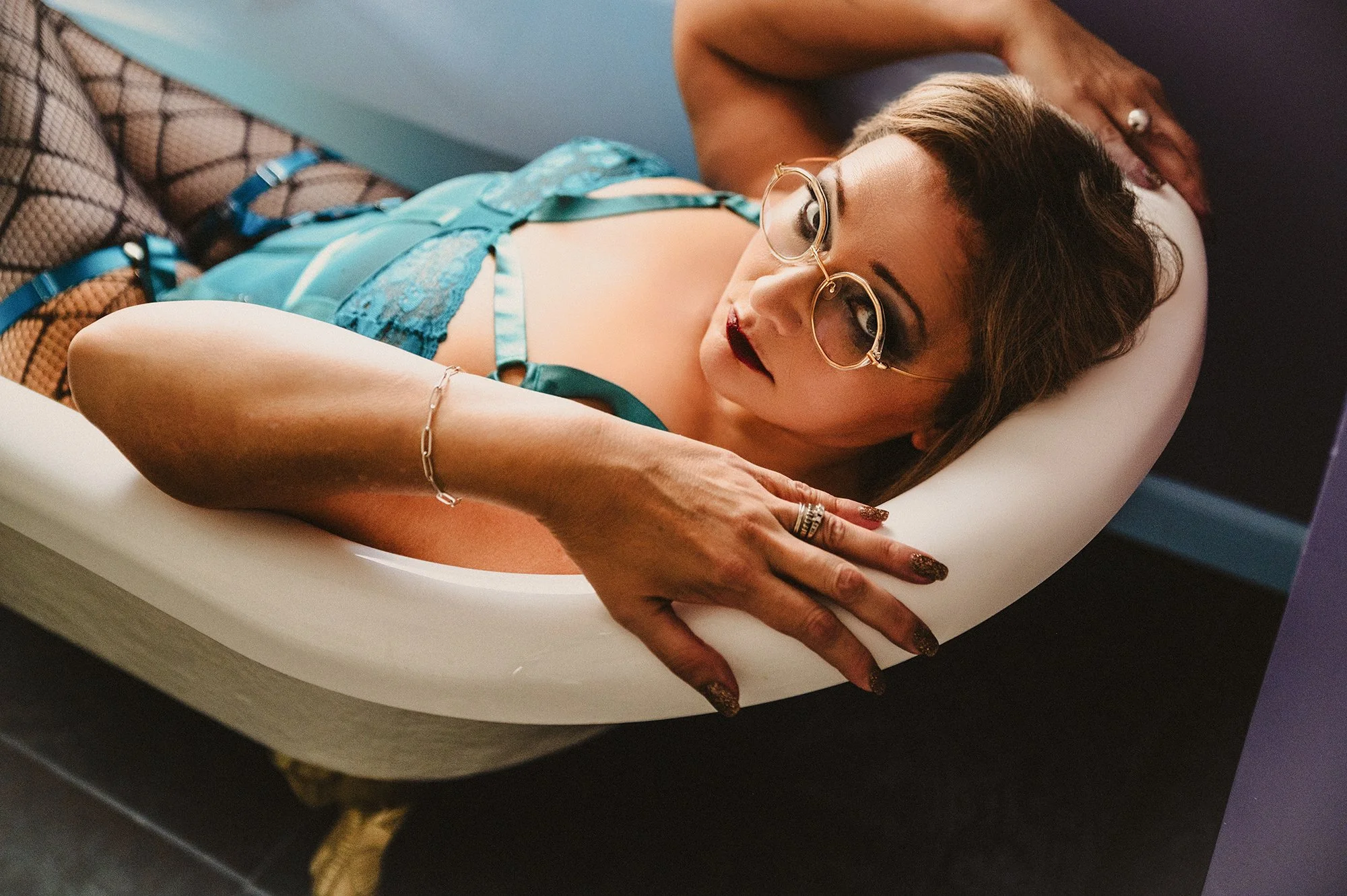 Woman posing in bathtub for boudoir session wearing aqua bodysuit and jewelry accessories photographed by Kaia at My Boudoir Atlanta.