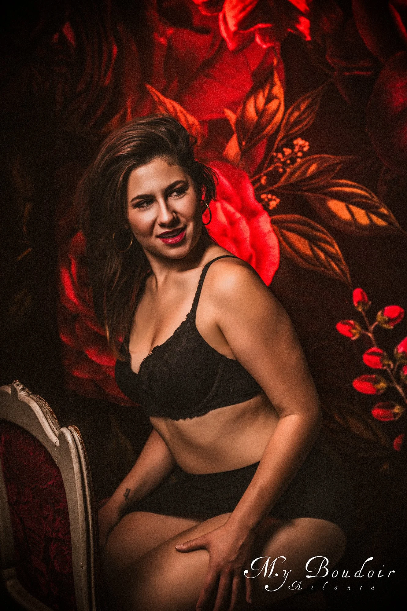 Woman in black lingerie posing against a floral wallpaper backdrop.