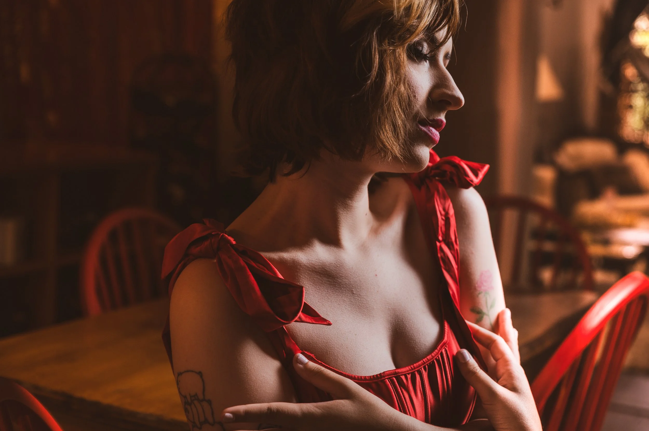 Woman in a red dress with tattoo on arm sitting in a dimly lit room with red chairs.