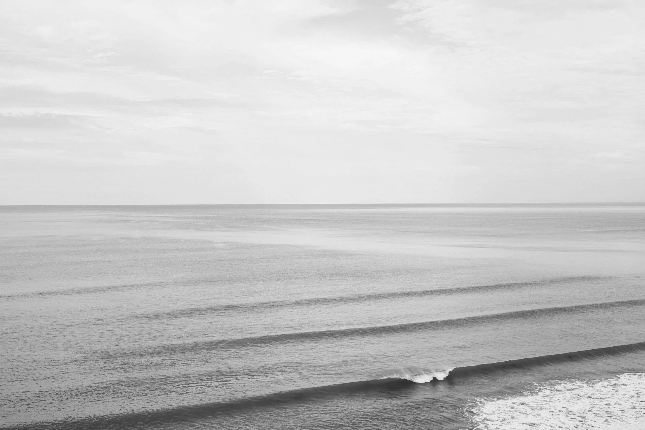 Black and white photo of the ocean on the Central Coast with gentle waves and a cloudy sky.