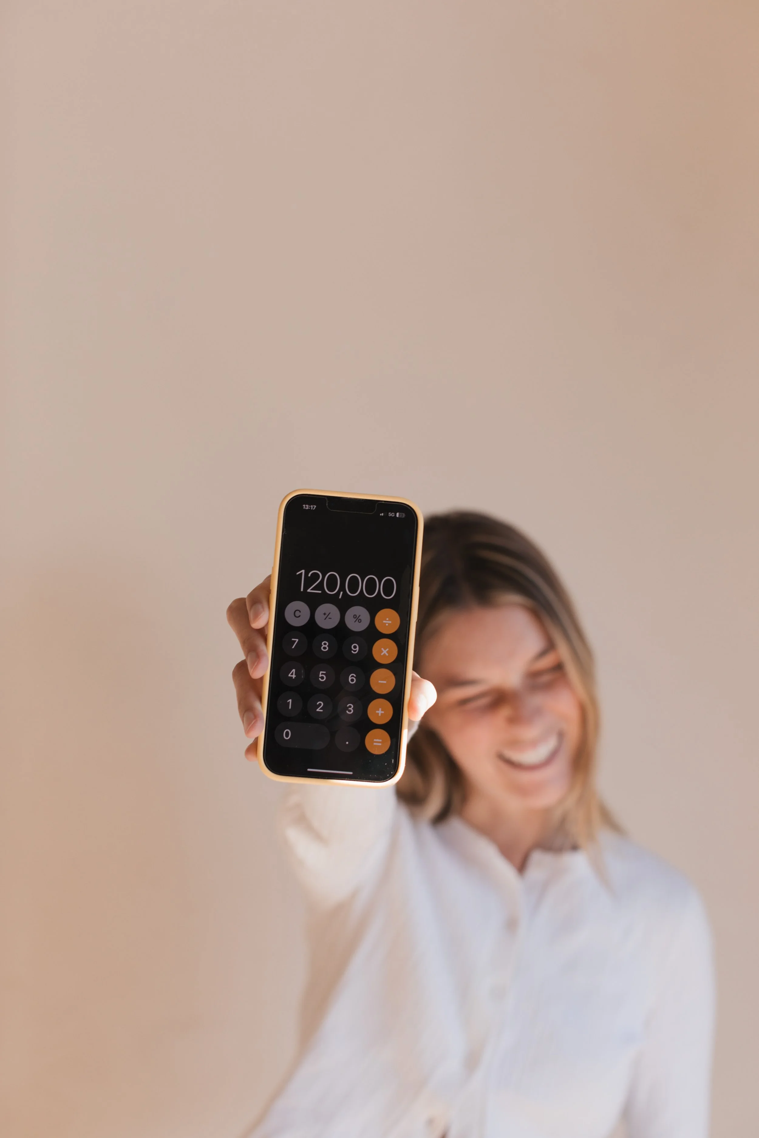 A woman smiling and showing a smartphone with the number 120,000 on the screen.