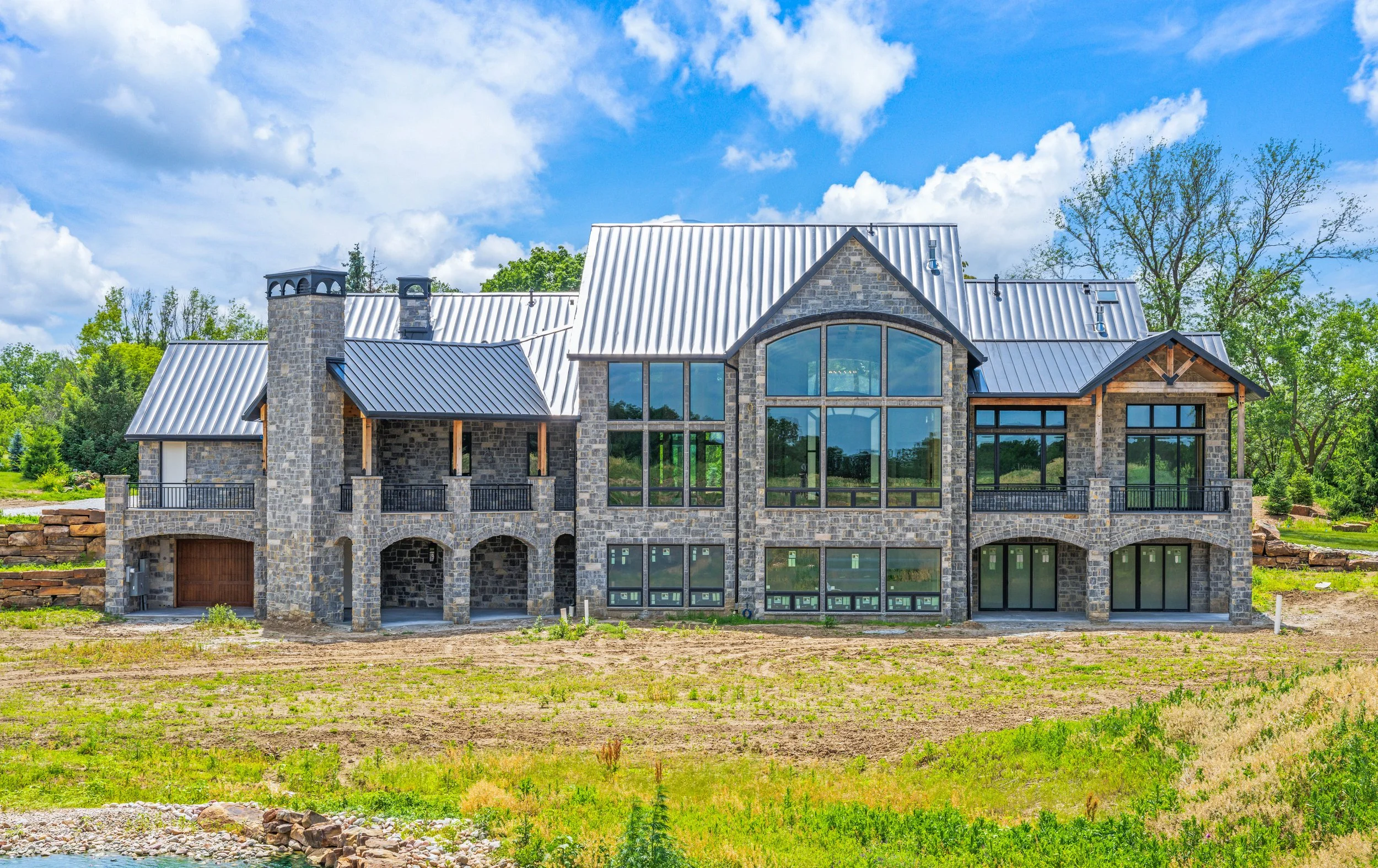 Custom home construction in progress showing stone exterior and timber framing before landscaping