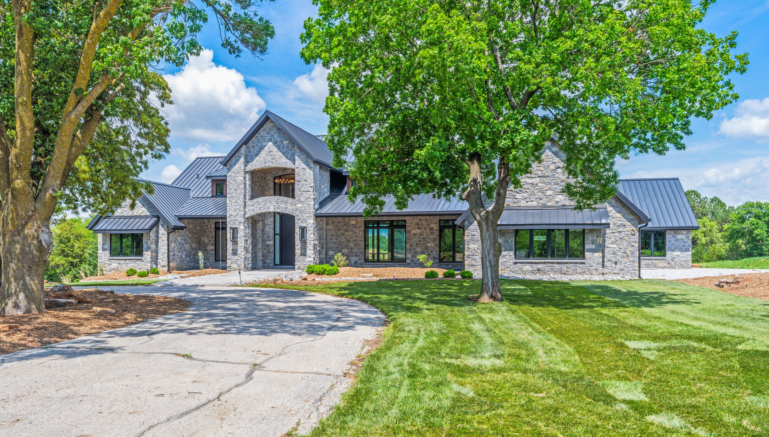 Completed custom stone home exterior with mature landscaping and paved driveway