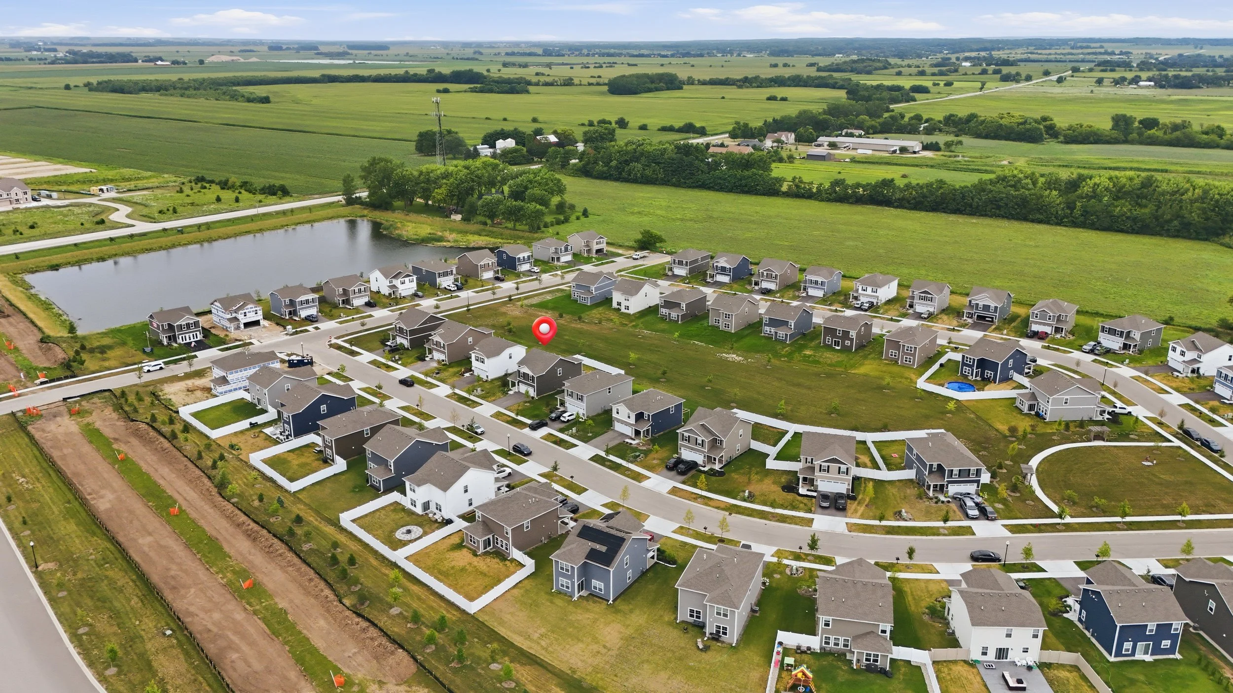 Aerial drone photo of a new construction neighborhood in Hampshire, Illinois, showing the home’s lot, a nearby pond, and open farmland