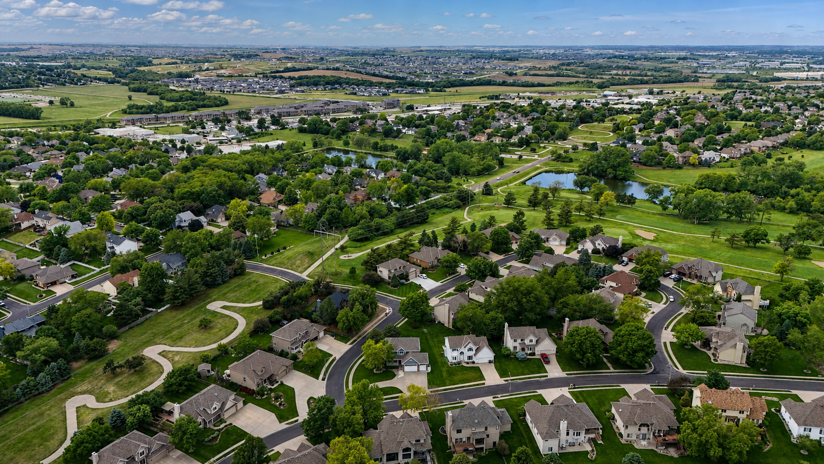 Aerial drone photo of a residential neighborhood showing home lots, streets, and surrounding green space